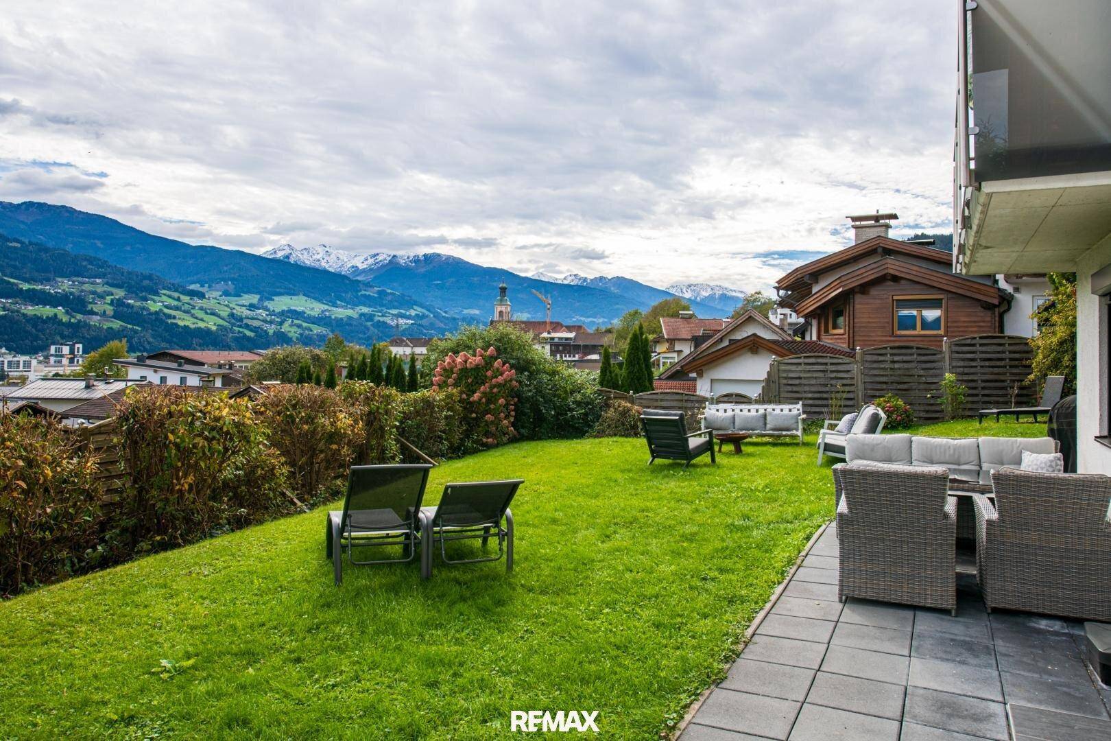 Gepflegter Garten mit Sitzgelegenheiten und weitem Blick auf die Berge und die Stadt.