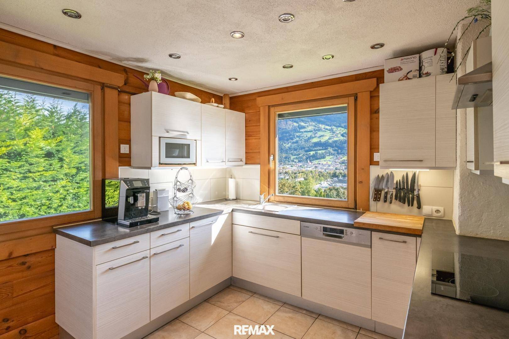 Funktionale Küche mit weißen Schränken, Holzwänden und einem Fenster mit Blick ins Grüne.