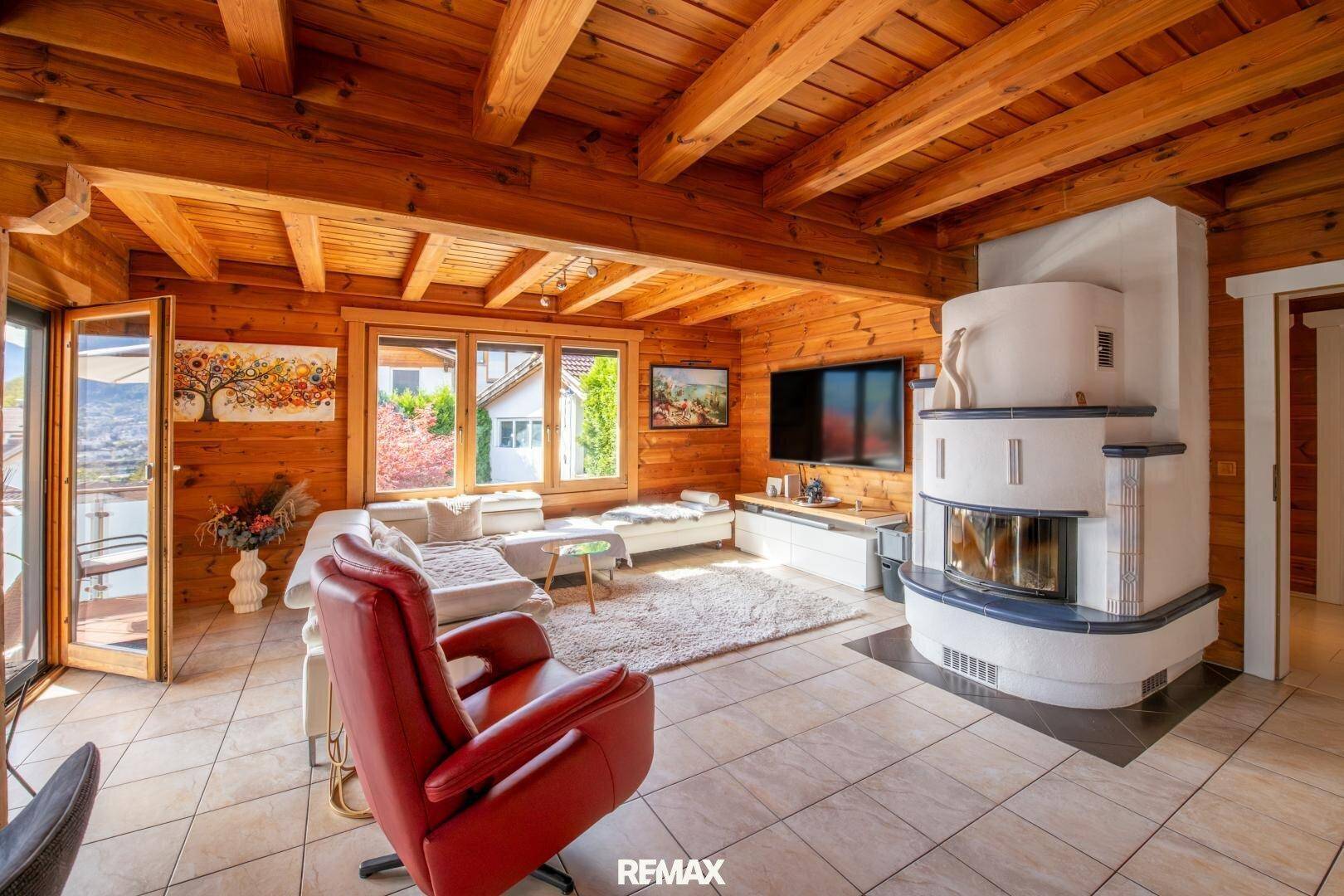 Helles Wohnzimmer mit Holzwänden, Fliesenboden und einem traditionellen Kachelofen.