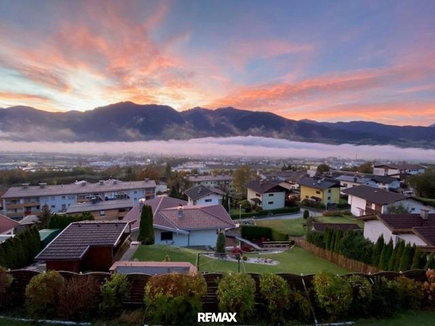 Malerischer Sonnenaufgang über dem Tal mit Bergen und Häusern in der Ferne.
