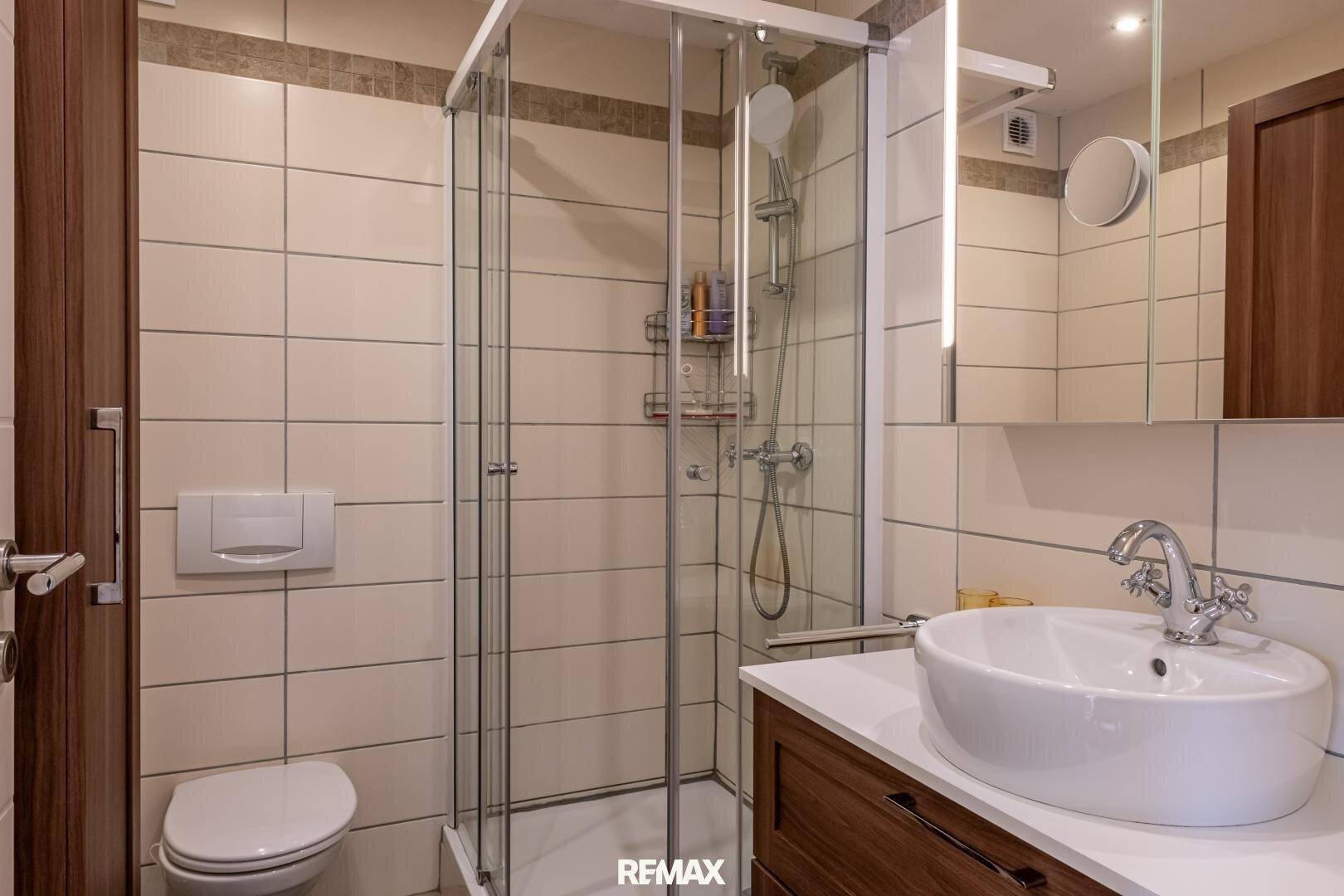 Helles Badezimmer mit Duschkabine, Toilette und modernem Waschbecken.