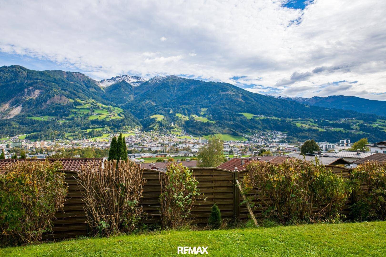 Panoramablick auf die Berge und eine Stadt, gesehen über eine Hecke.