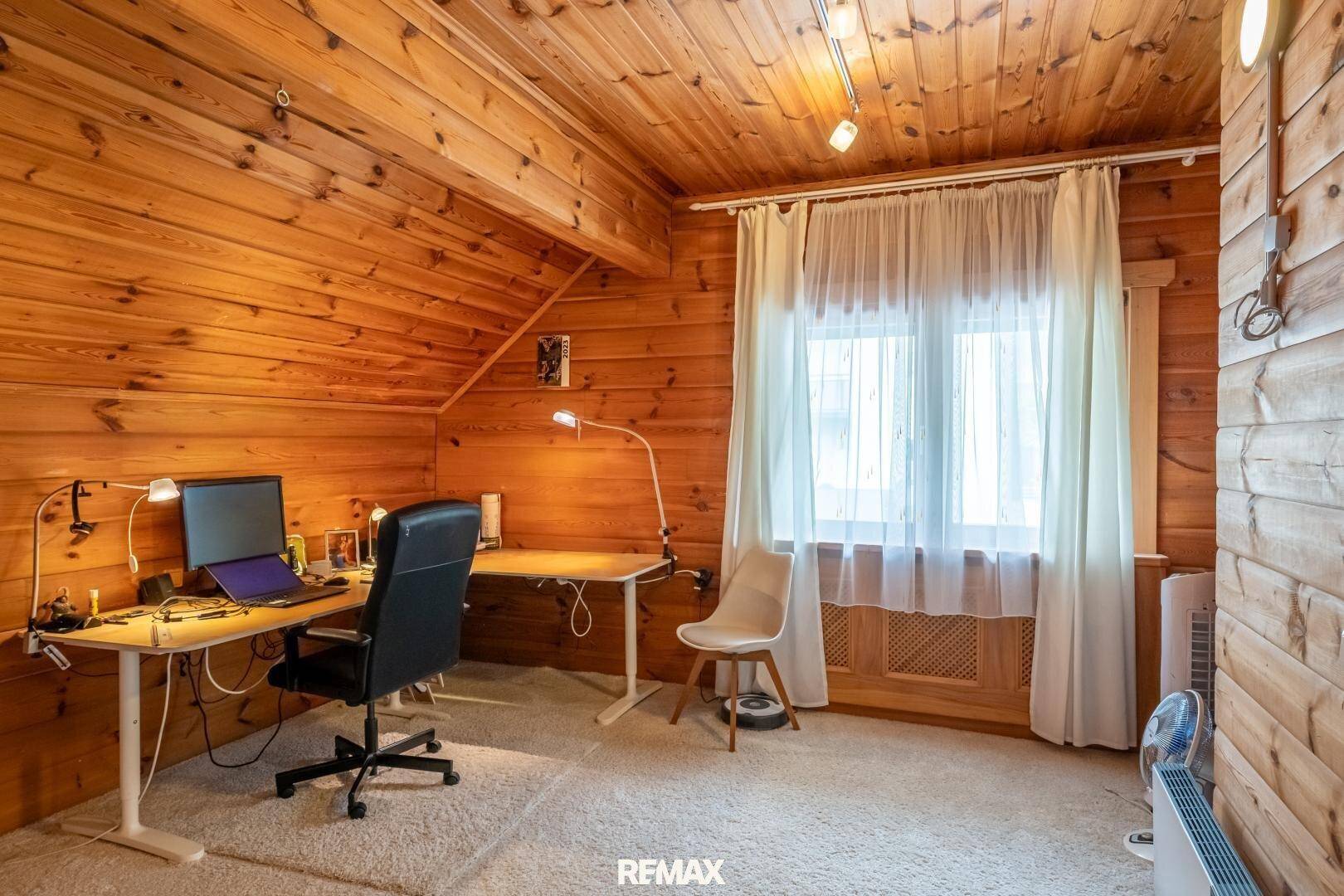 Geräumiges Arbeitszimmer mit Holzwänden, Teppichboden und Dachschräge.