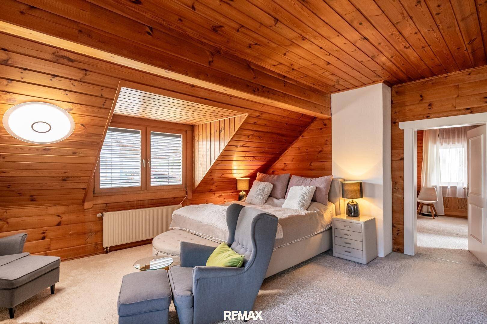 Gemütliches Schlafzimmer mit Holzwänden, Teppichboden und Dachschräge.