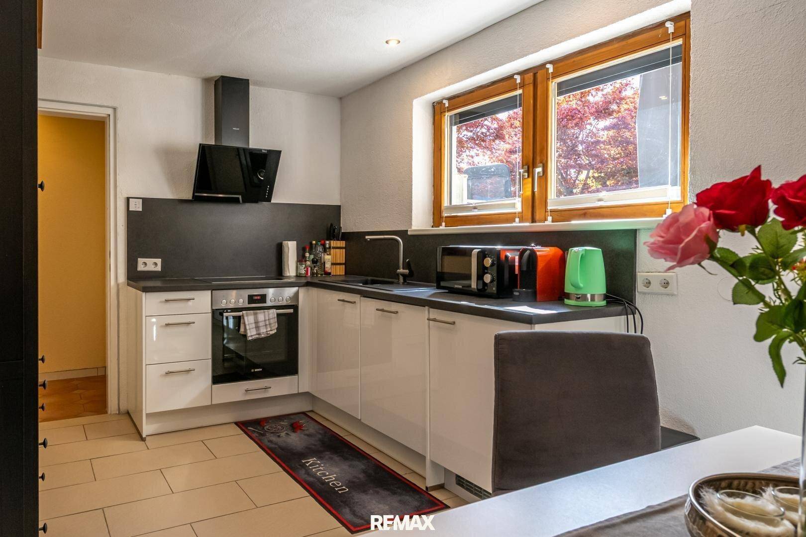 Moderne Küche mit weißen Hochglanzfronten, dunkler Arbeitsplatte und Essbereich.