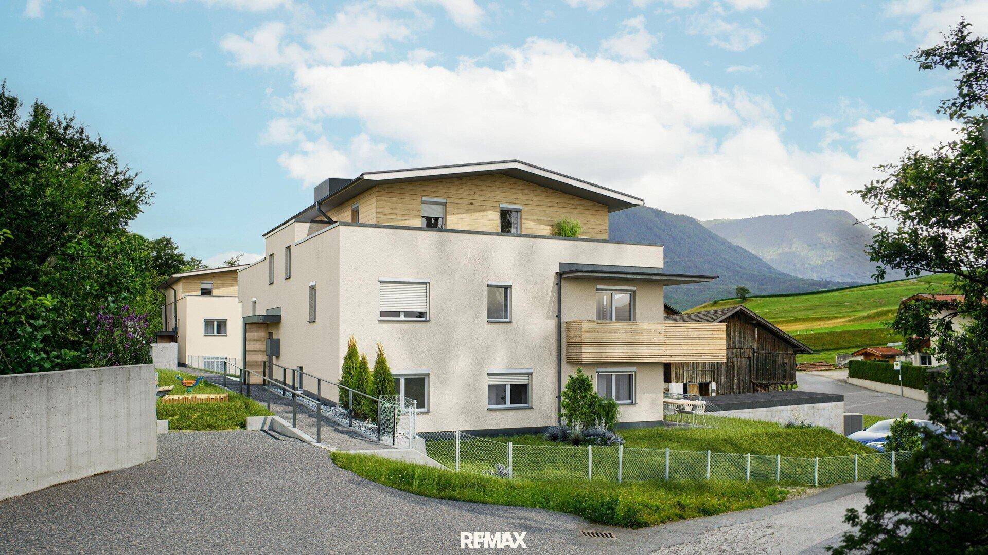 Neubauwohngebäude mit barrierefreier Rampe und Blick auf die umliegende Natur und Berge.