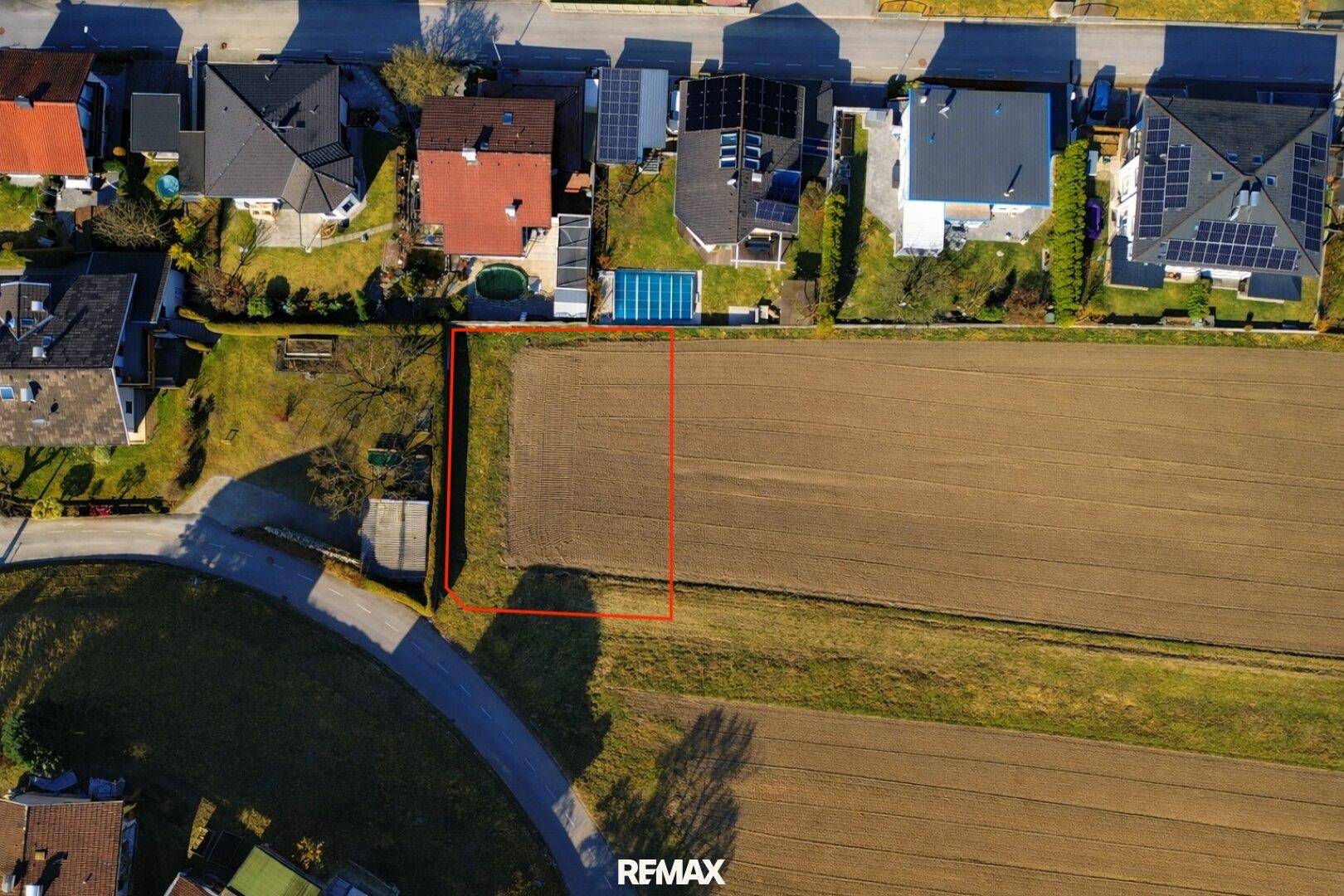 Luftaufnahme eines Baugrundstücks mit roter Markierung, umgeben von Wohnhäusern und Feldern.