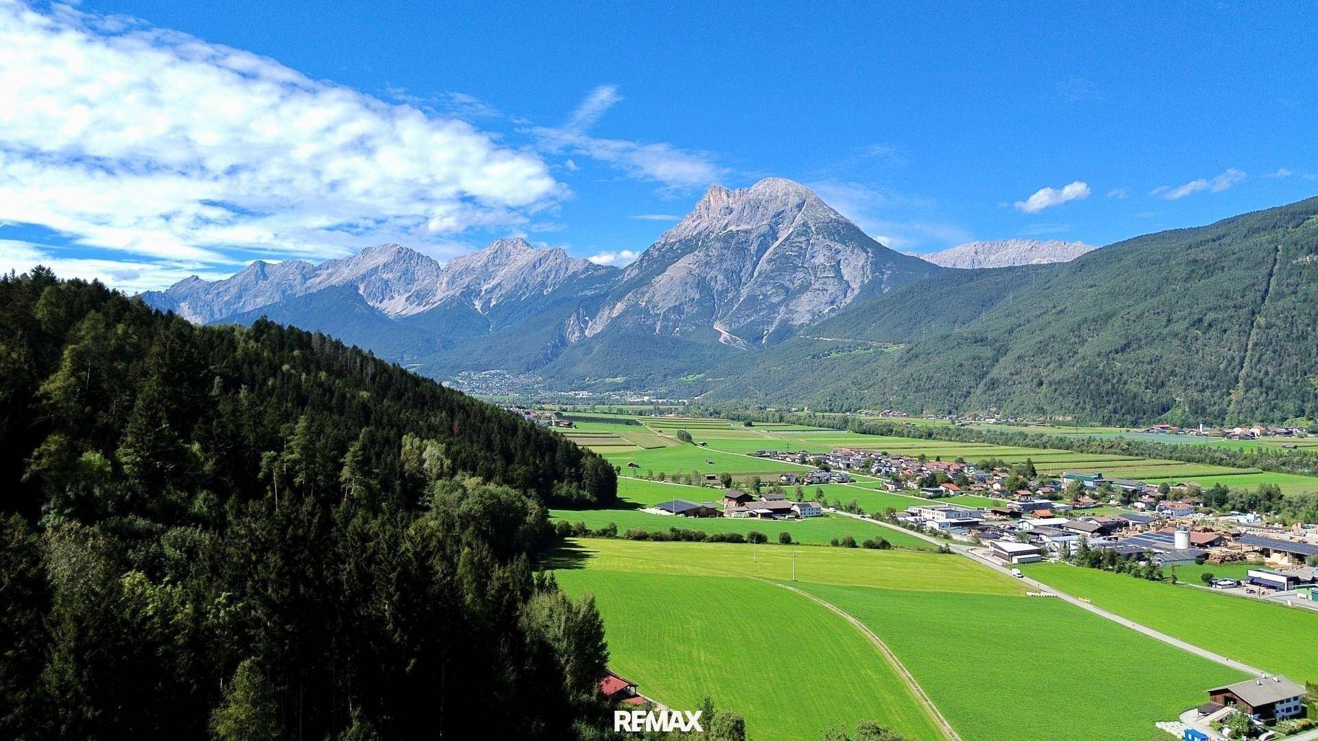 Malerische Landschaftsaufnahme eines weiten Tals mit grünen Feldern und imposanten Bergketten.