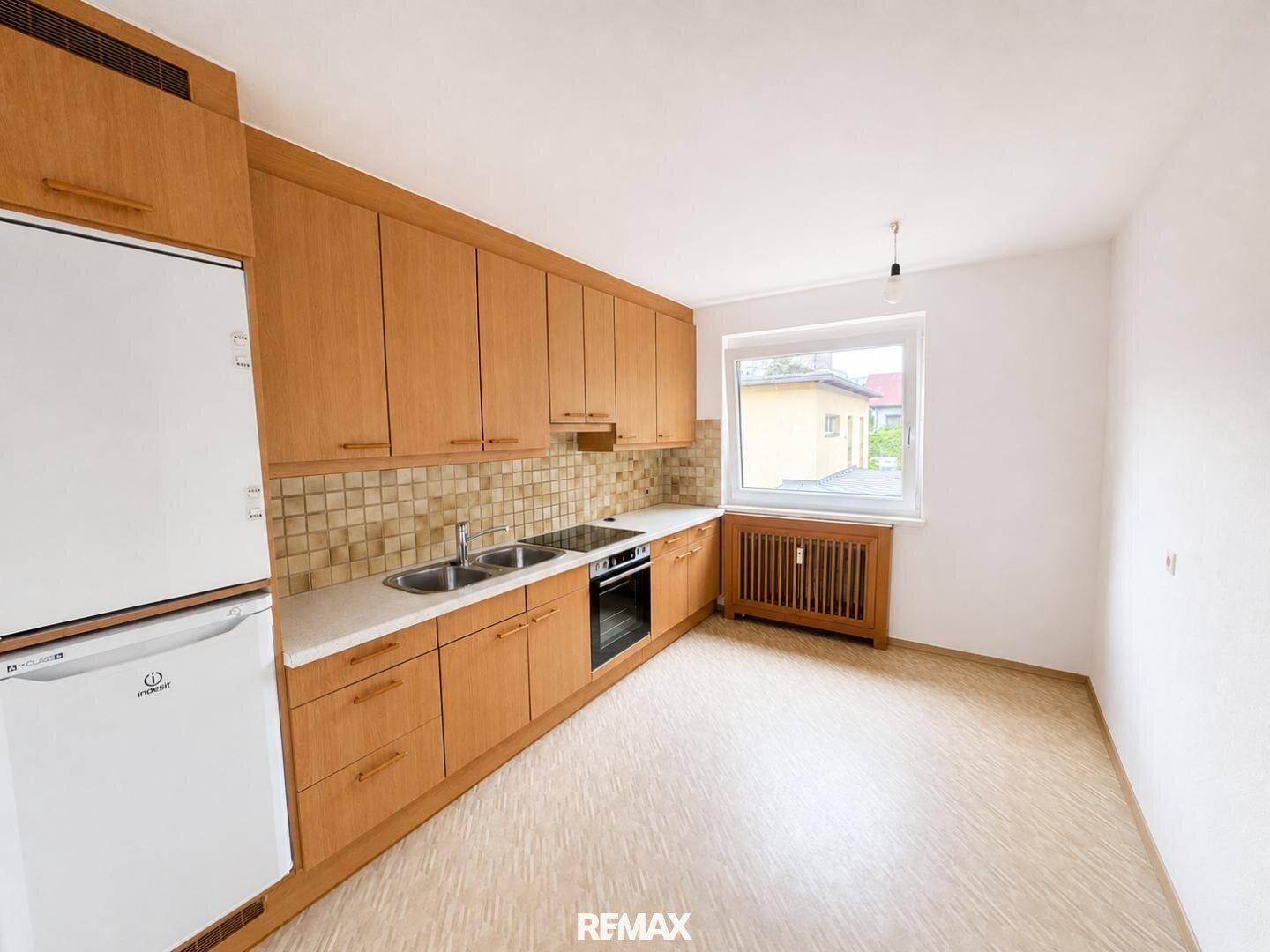 Küche mit Holzschränken, integrierten Geräten und Fenster, bietet ausreichend Arbeits- und Stauraum.