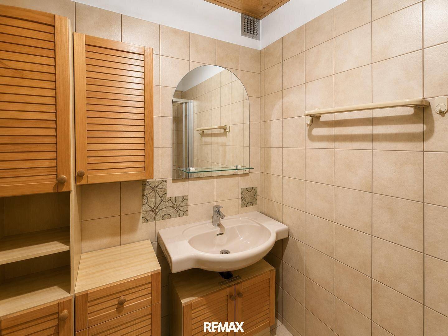 Badezimmer mit beigefarbenen Fliesen, Einzelwaschbecken und Holzschränken, bietet Stauraum.
