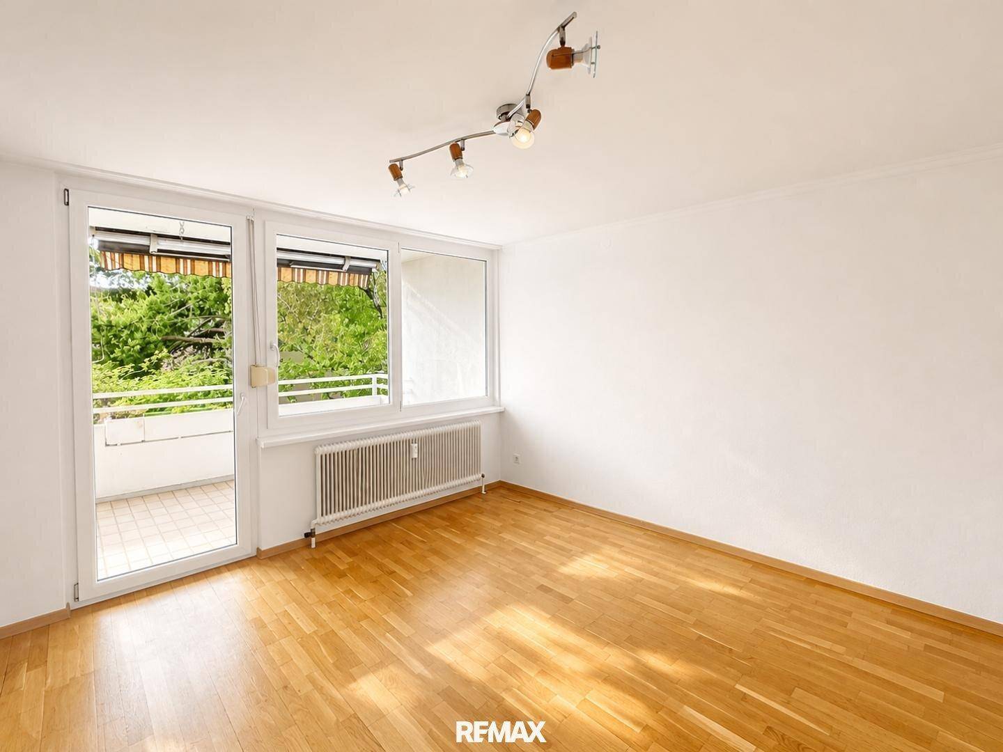 Helles Wohnzimmer mit Parkettboden, großen Fenstern und Zugang zum Balkon, bereit zur individuellen Gestaltung.