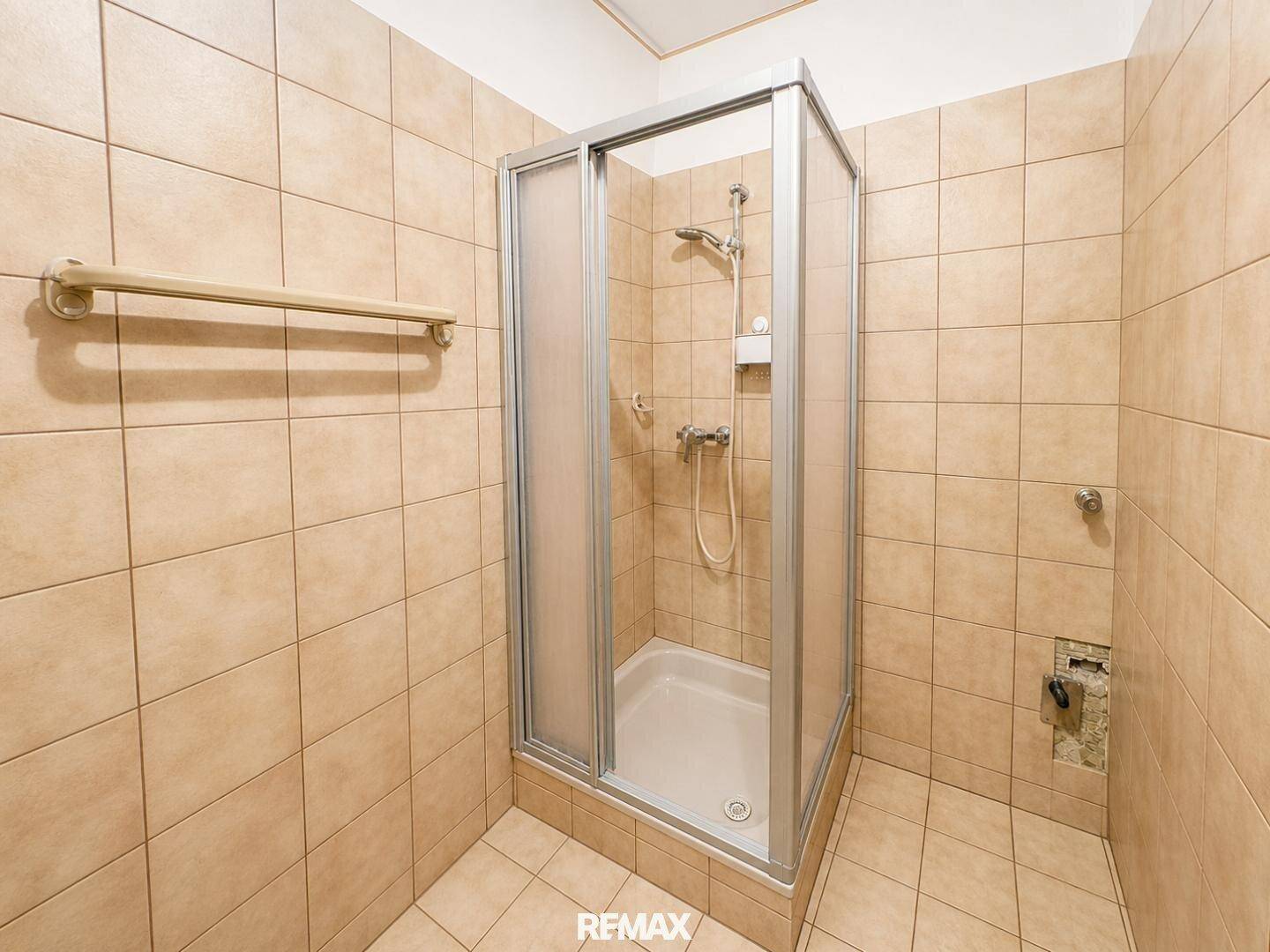 Funktionales Badezimmer mit beigefarbenen Fliesen und einer praktischen Duschkabine, in gutem Zustand.