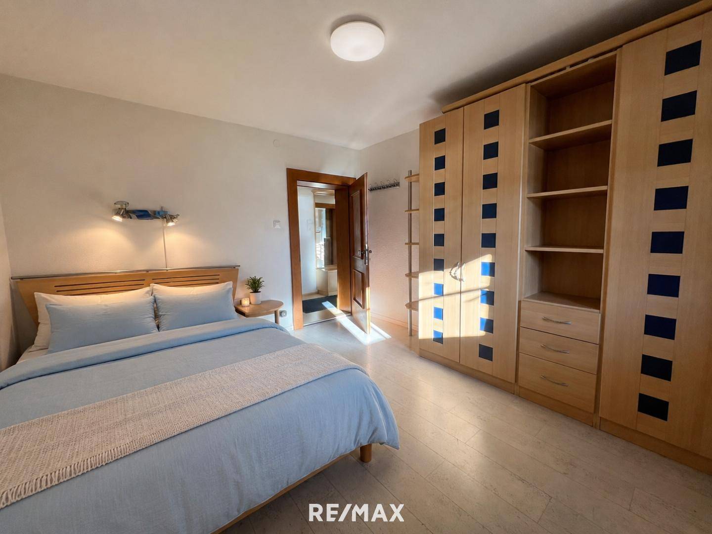 Helles Schlafzimmer mit Holzboden, blauem Bett und einem großen Einbauschrank.