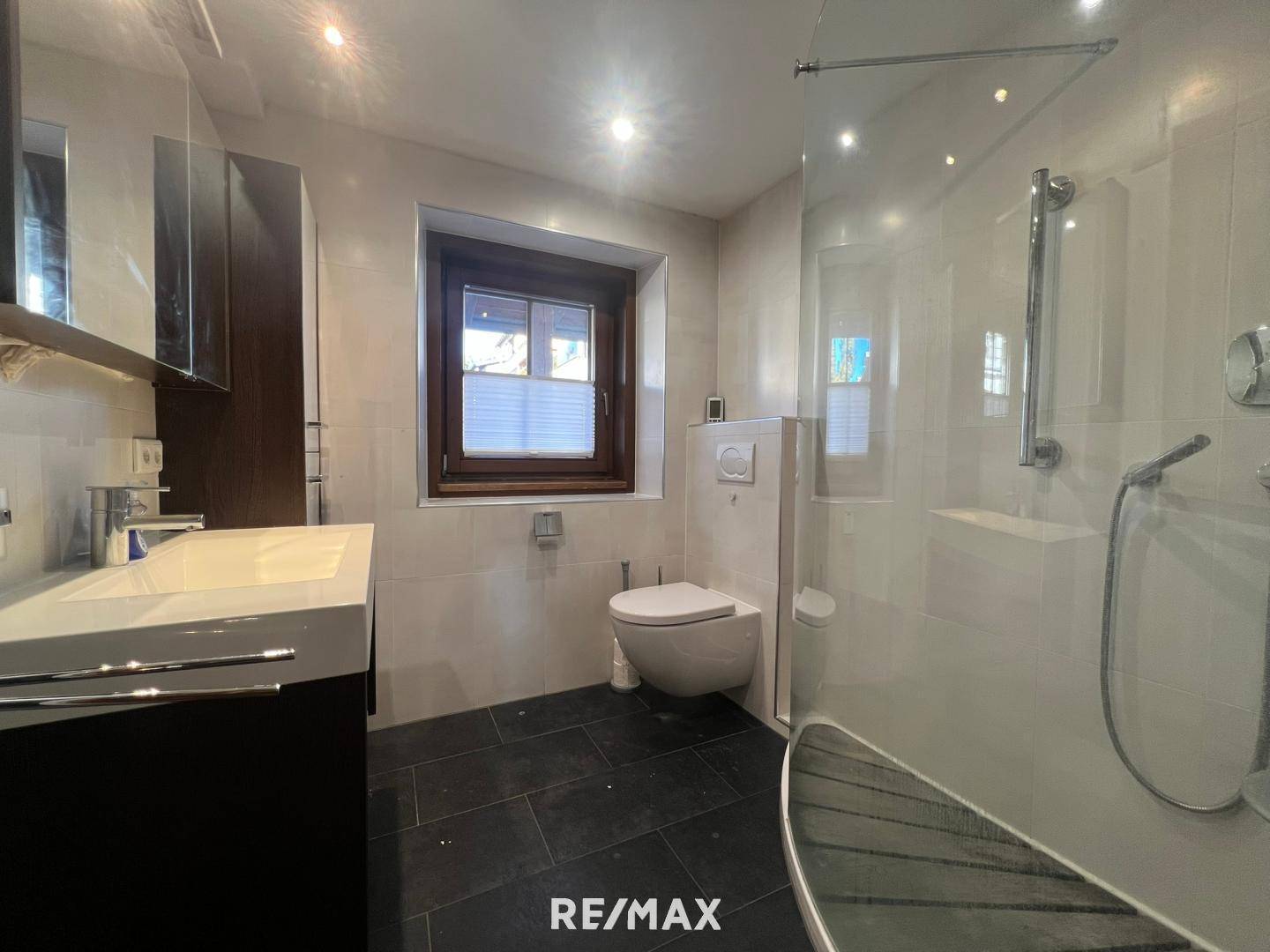 Modernes Badezimmer mit begehbarer Dusche, Wand-WC, Waschtisch und Fenster.
