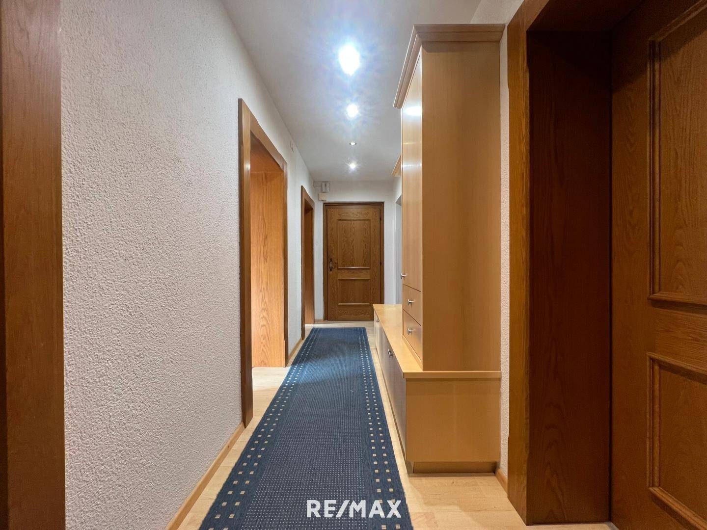 Heller Flur mit Holztüren, Einbauschrank und einem blauen Teppichläufer.