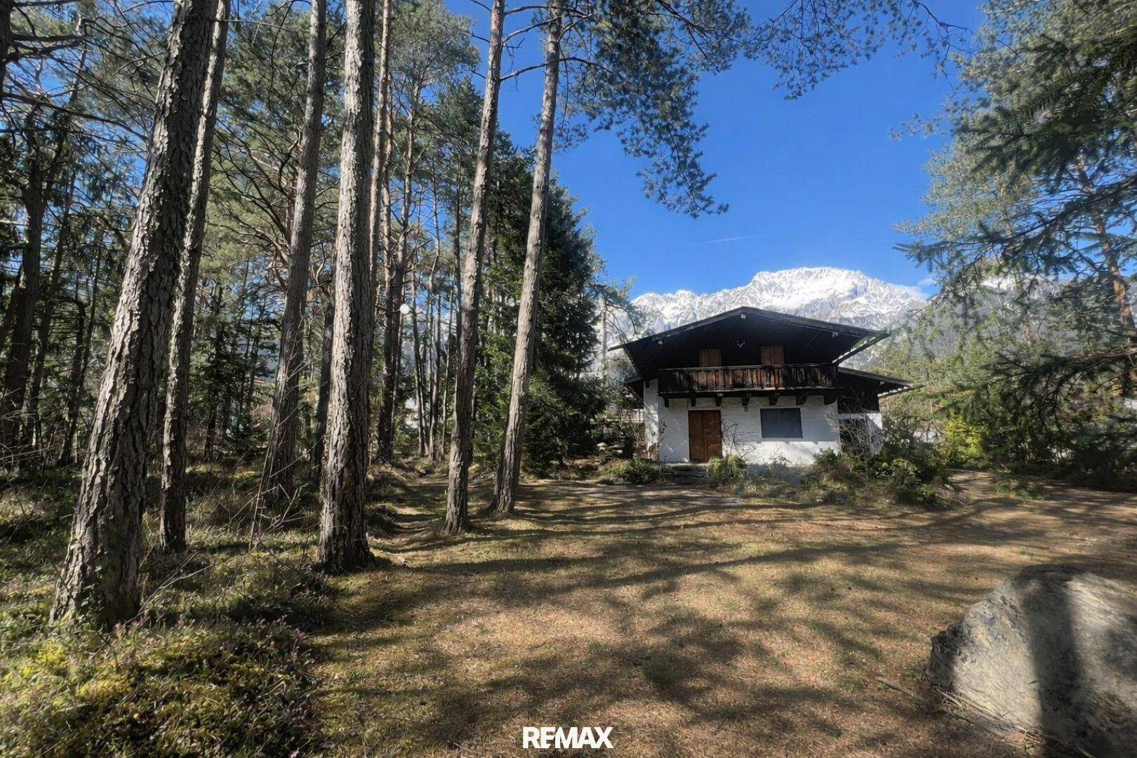 Ein idyllisches Haus umgeben von hohen Bäumen und einem weiten Blick auf schneebedeckte Berge.