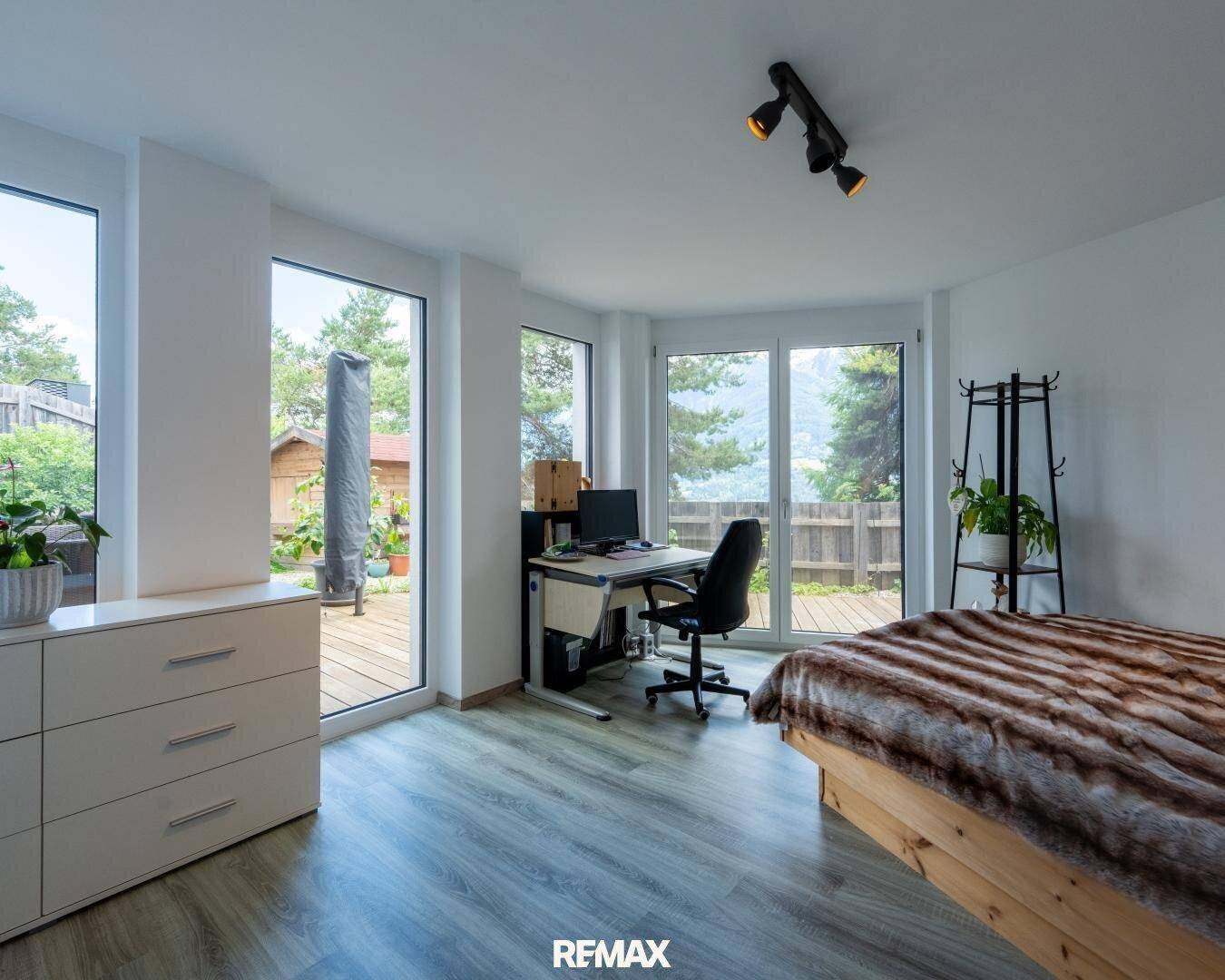 Geräumiges Schlafzimmer mit Holzbett, Schreibtisch und großen Fenstern mit Blick auf die Natur.