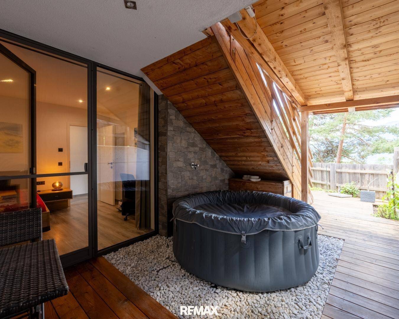 Überdachte Terrasse mit Whirlpool und Holzboden, direkt zugänglich von einem Innenraum.