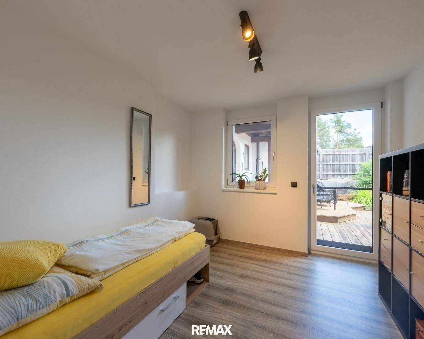 Helles Schlafzimmer mit Einzelbett, Laminatboden und direktem Zugang zu einer Außenterrasse.