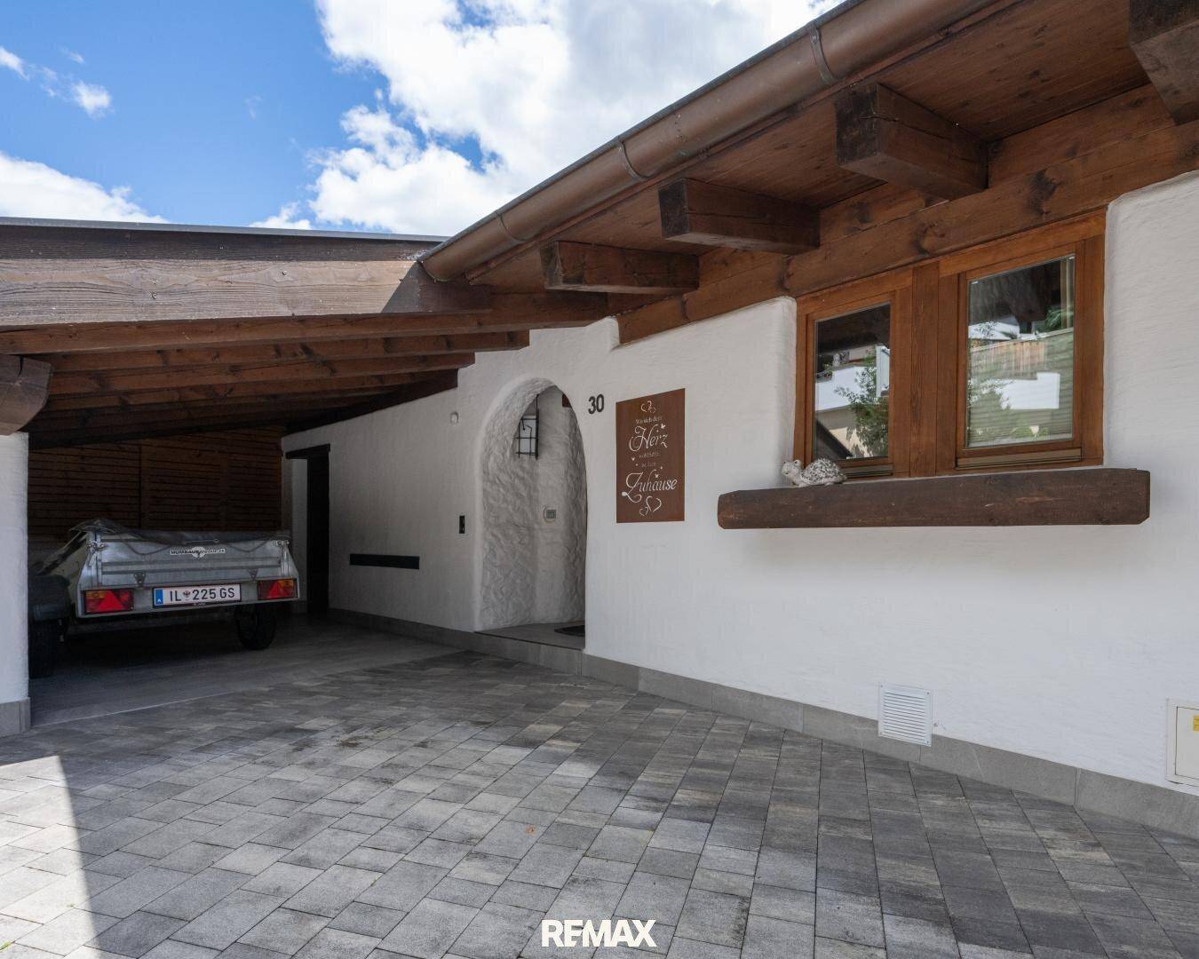 Traditioneller Eingangsbereich mit Holzelementen und überdachtem Carport für Fahrzeuge.
