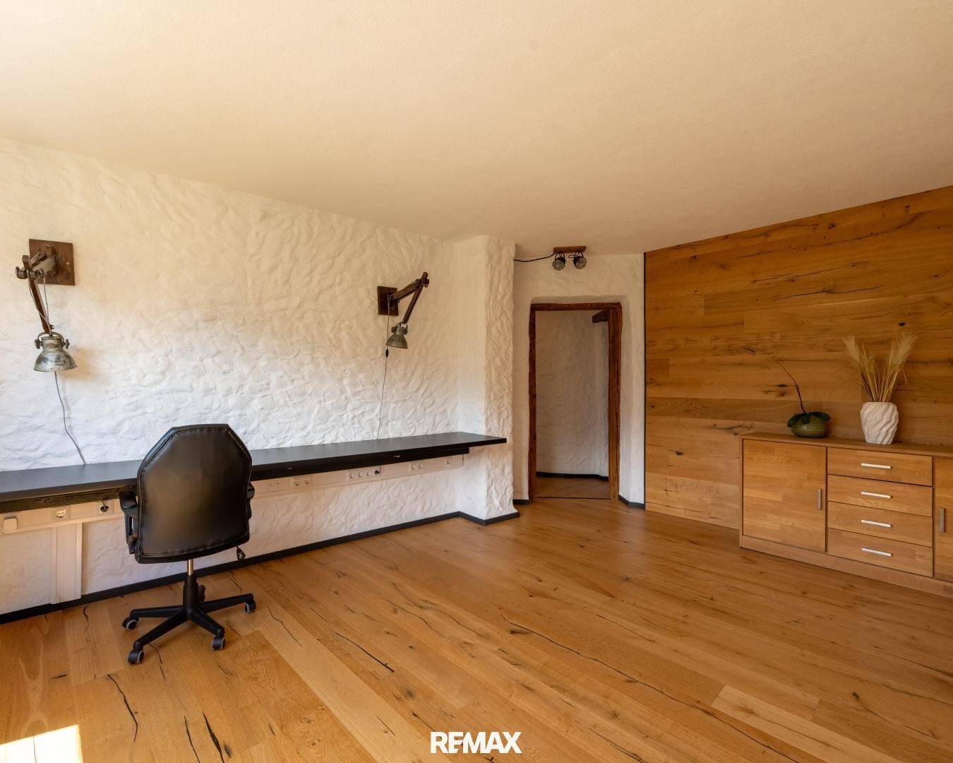 Geräumiges Arbeitszimmer mit Holzboden, weiß getünchten Wänden und einer langen Arbeitsplatte.