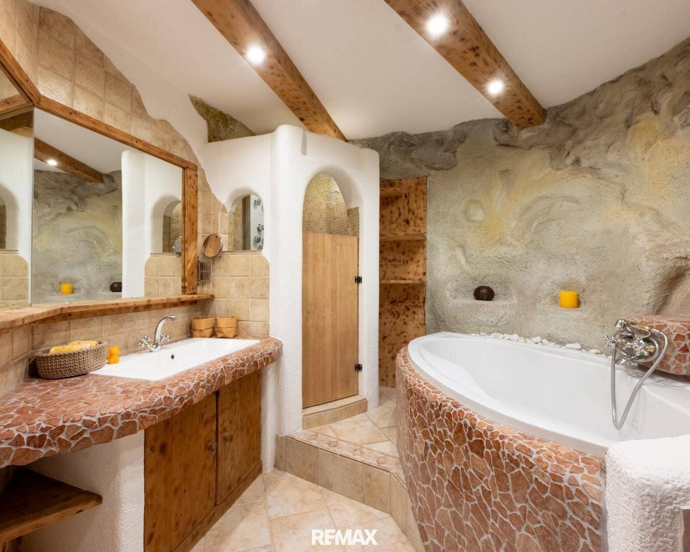 Einzigartiges Badezimmer im alpinen Stil mit freistehender Badewanne und rustikalen Stein- und Holzelementen.