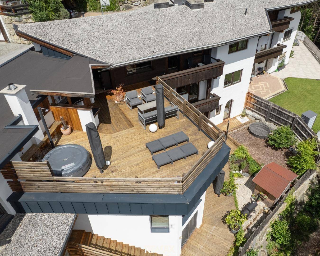 Luftaufnahme des Anwesens mit großer Holzterrasse, Whirlpool und Gartenbereich in alpiner Umgebung.