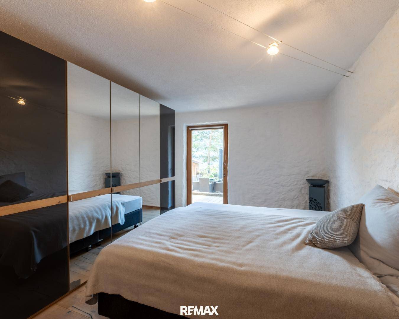 Schlafzimmer mit großem Bett, Spiegelschränken und Zugang zu einem kleinen Balkon oder Außenbereich.