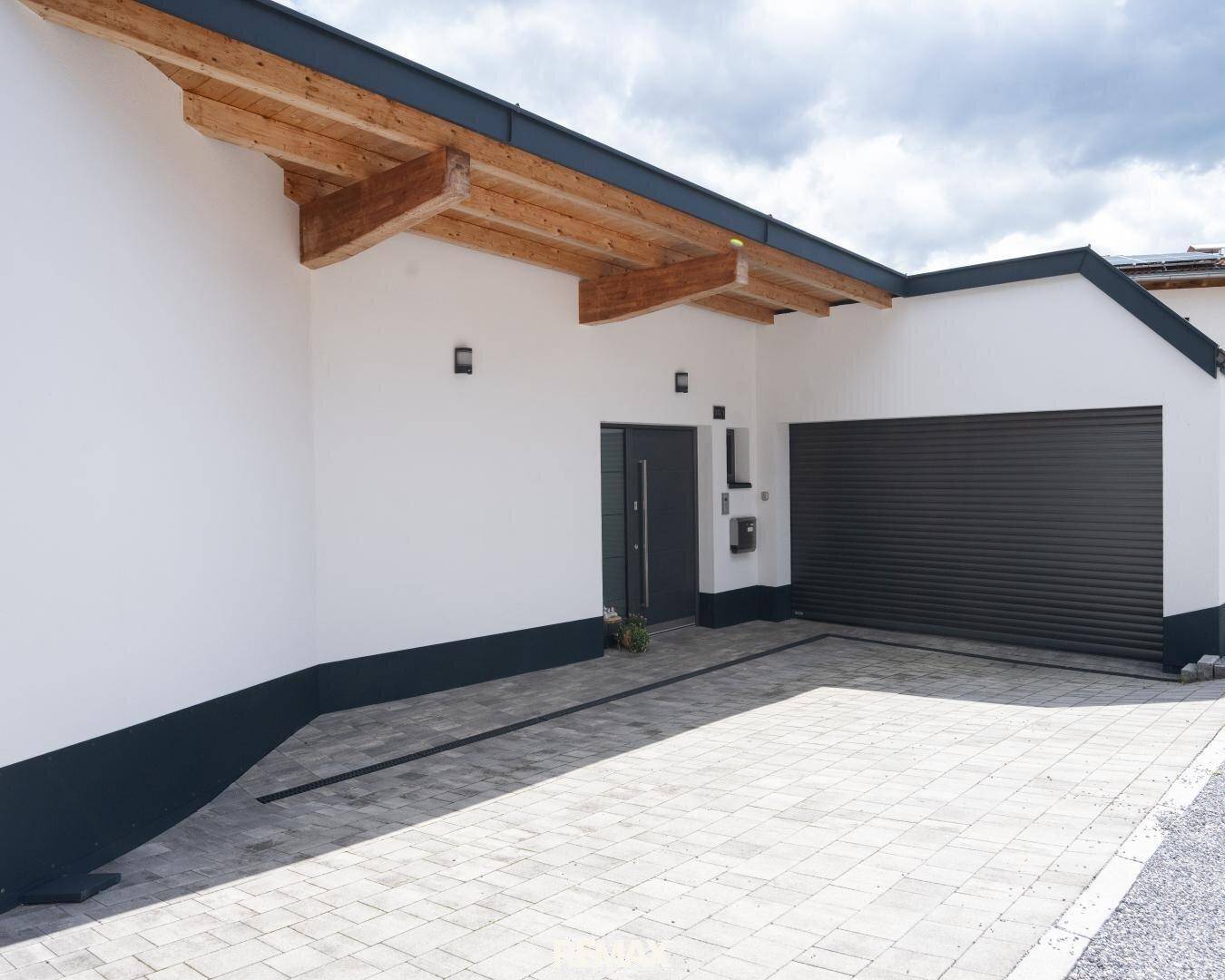 Moderne Hausfassade mit Eingangsbereich, Garagentor und gepflasterter Auffahrt.