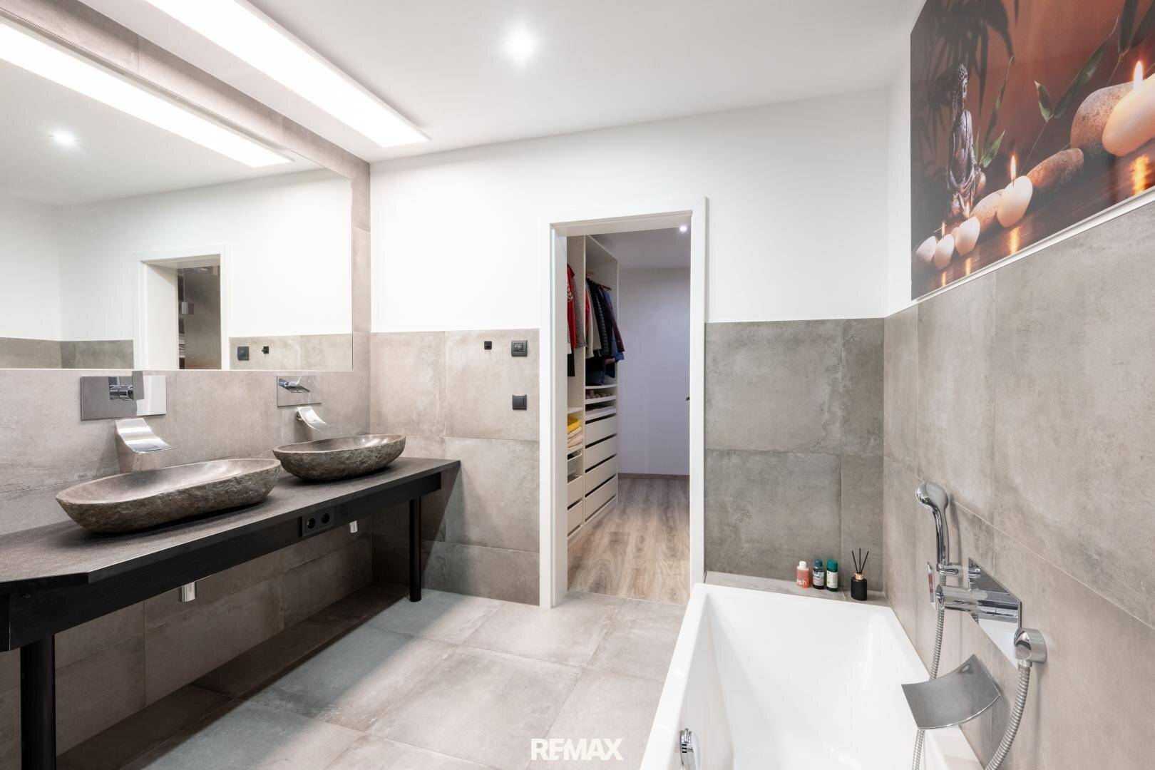Modernes Badezimmer mit Doppelwaschbecken, Badewanne und begehbarem Kleiderschrank im Hintergrund.