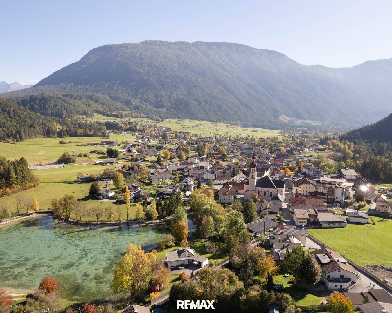 Weitläufige Luftaufnahme des malerischen Dorfes am See, eingebettet in eine Berglandschaft.
