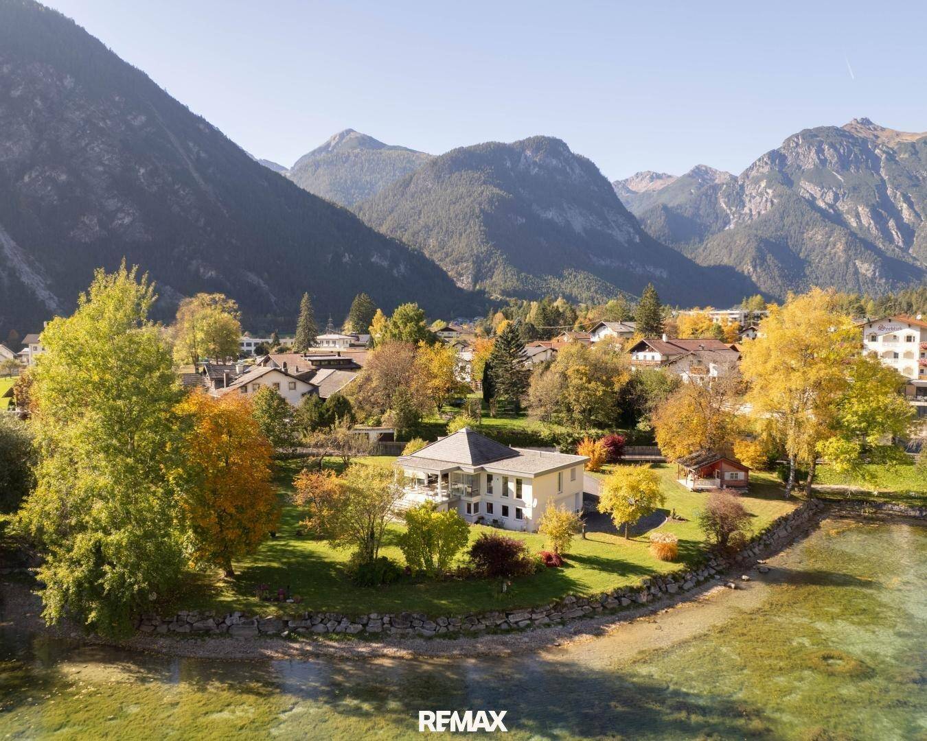 Weitläufige Luftaufnahme des Anwesens am Seeufer, umgeben von herbstlichen Bäumen und Bergen.