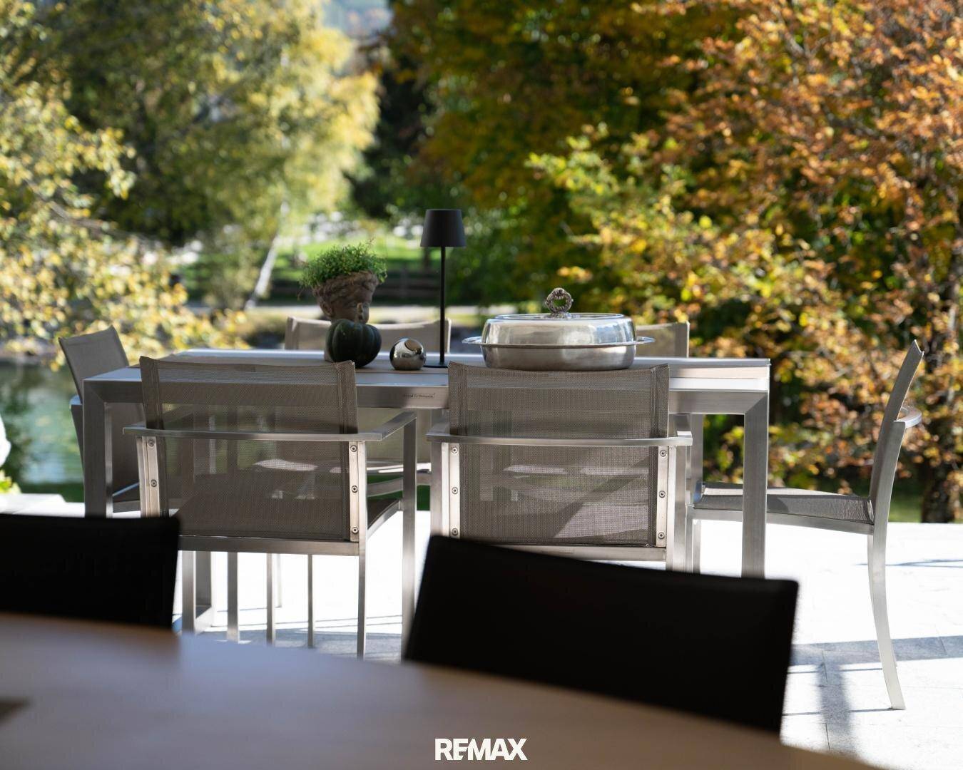 Detailaufnahme des Esstisches auf der Terrasse mit Blick auf die herbstliche Natur und das Wasser.