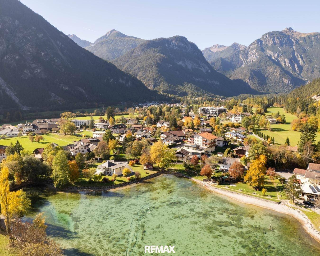 Panoramablick auf das Dorf am Seeufer, umgeben von majestätischen Bergen und grüner Natur.