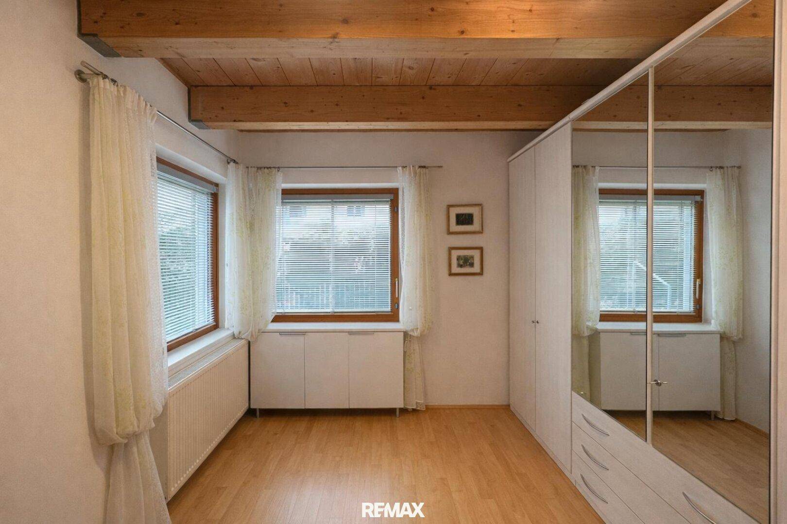 Geräumiges Zimmer mit Holzbalkendecke, großen Fenstern und Spiegelschränken.