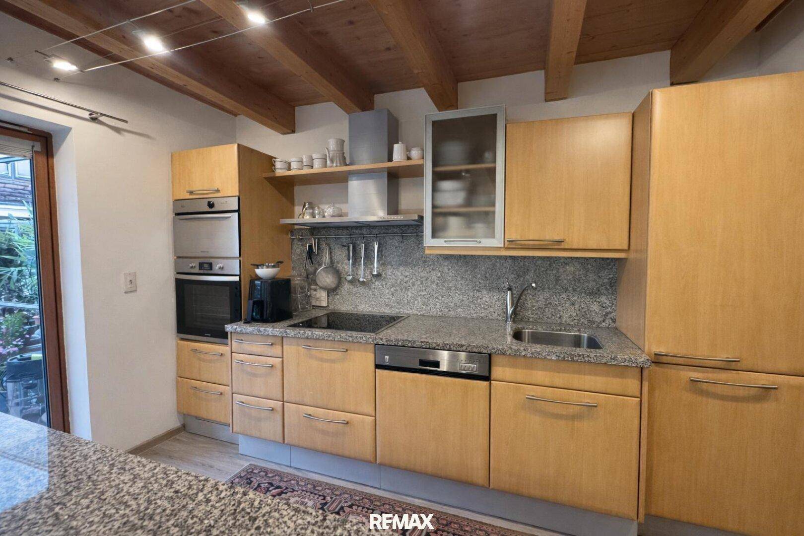 Funktionale Küche mit Holzschränken, Granitarbeitsplatte und modernen Einbaugeräten.