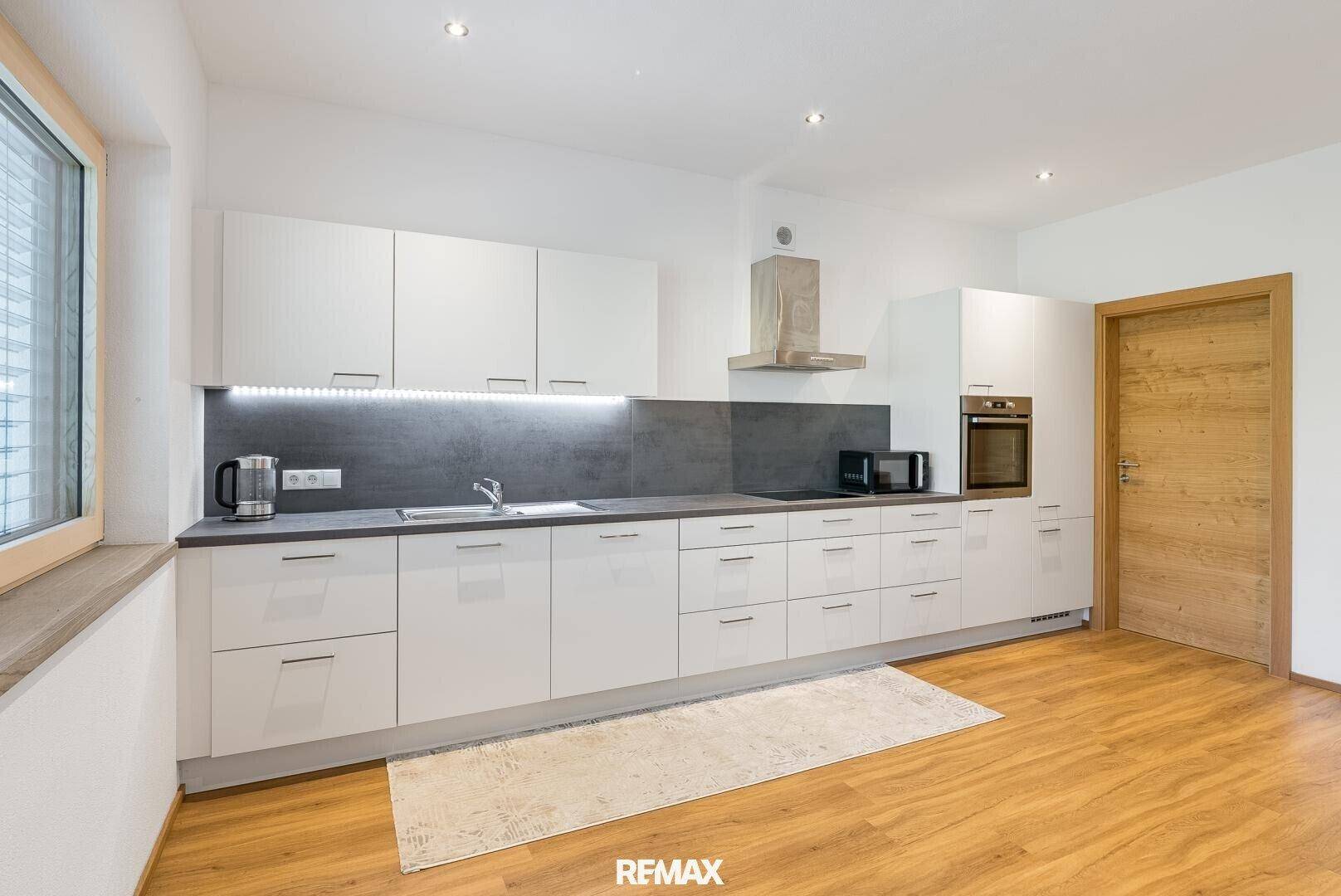 Funktionale Küche mit weißen Schränken, dunkler Arbeitsplatte und Laminatboden.