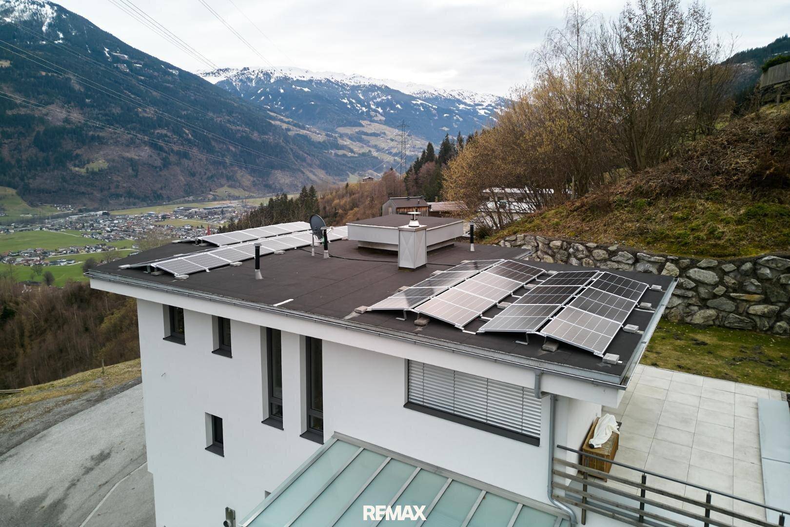 Luftaufnahme des Hauses mit Flachdach und Photovoltaikanlage in alpiner Umgebung.
