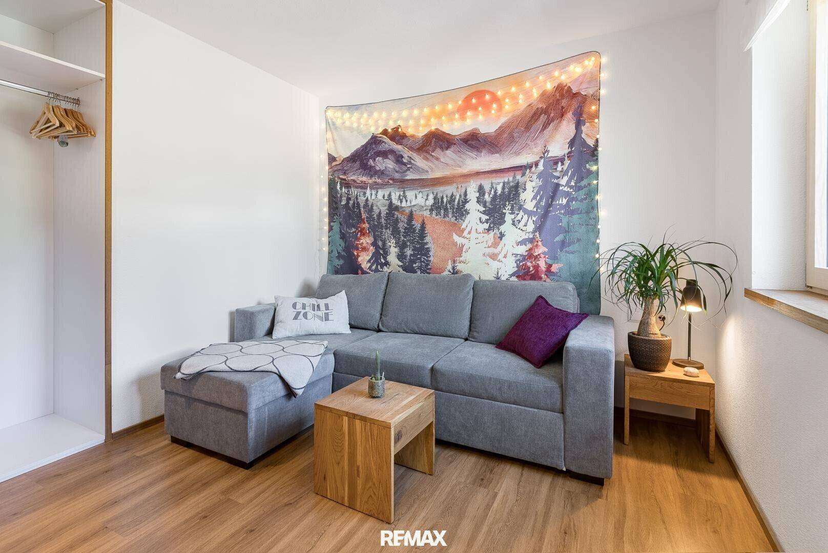 Gemütlicher Wohnbereich mit grauem Sofa, Holztisch und dekorativem Wandteppich.
