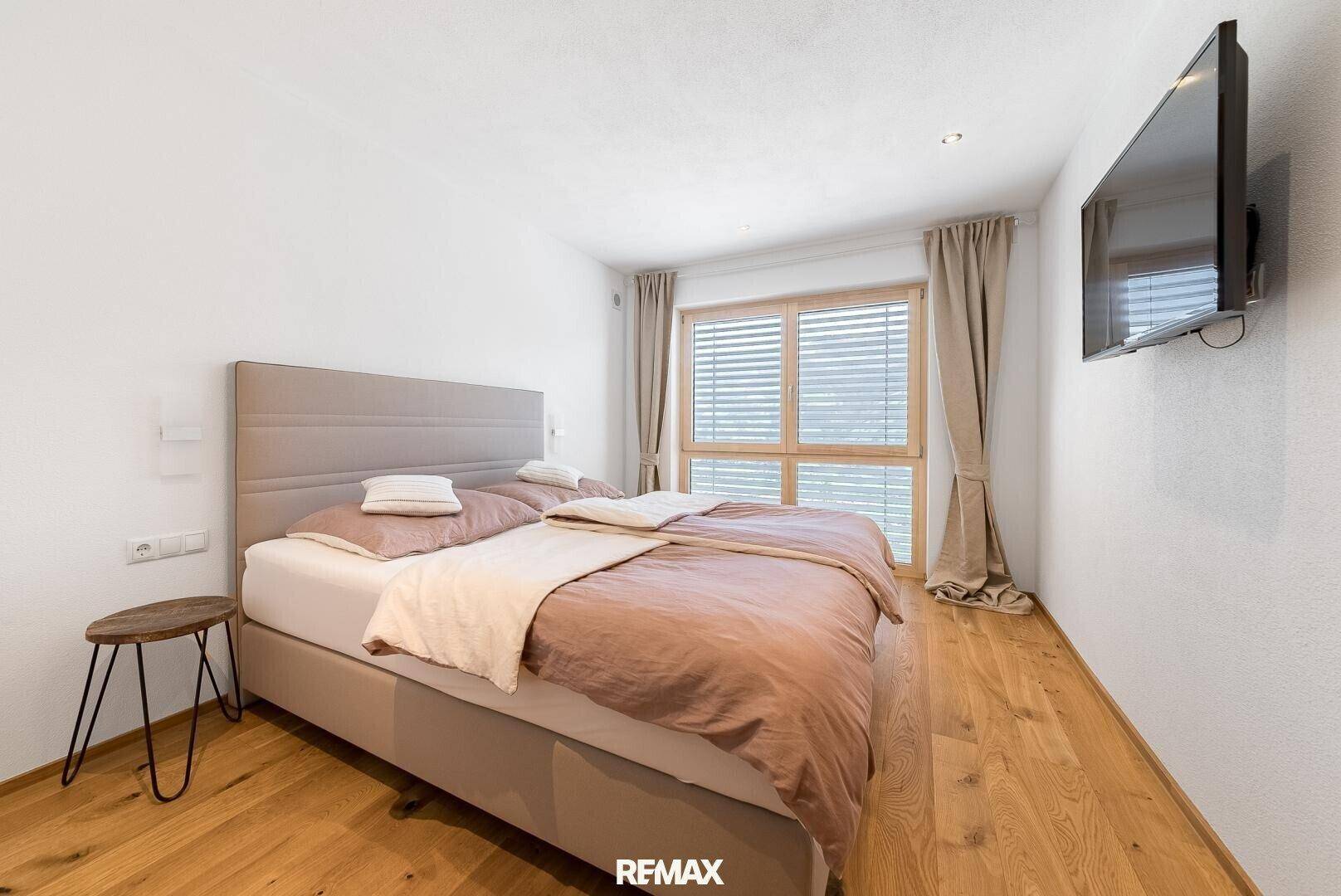 Gemütliches Schlafzimmer mit Doppelbett, Holzboden und Wandfernseher.