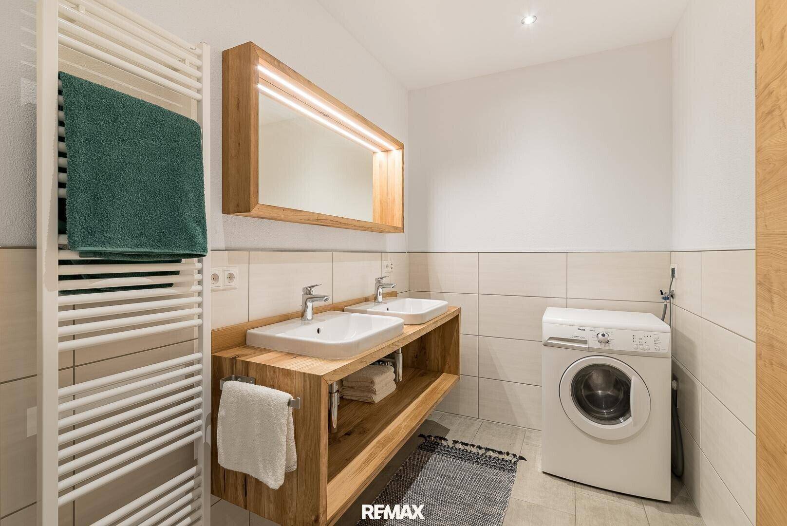 Modernes Badezimmer mit Doppelwaschbecken, beheiztem Handtuchhalter und Waschmaschine.
