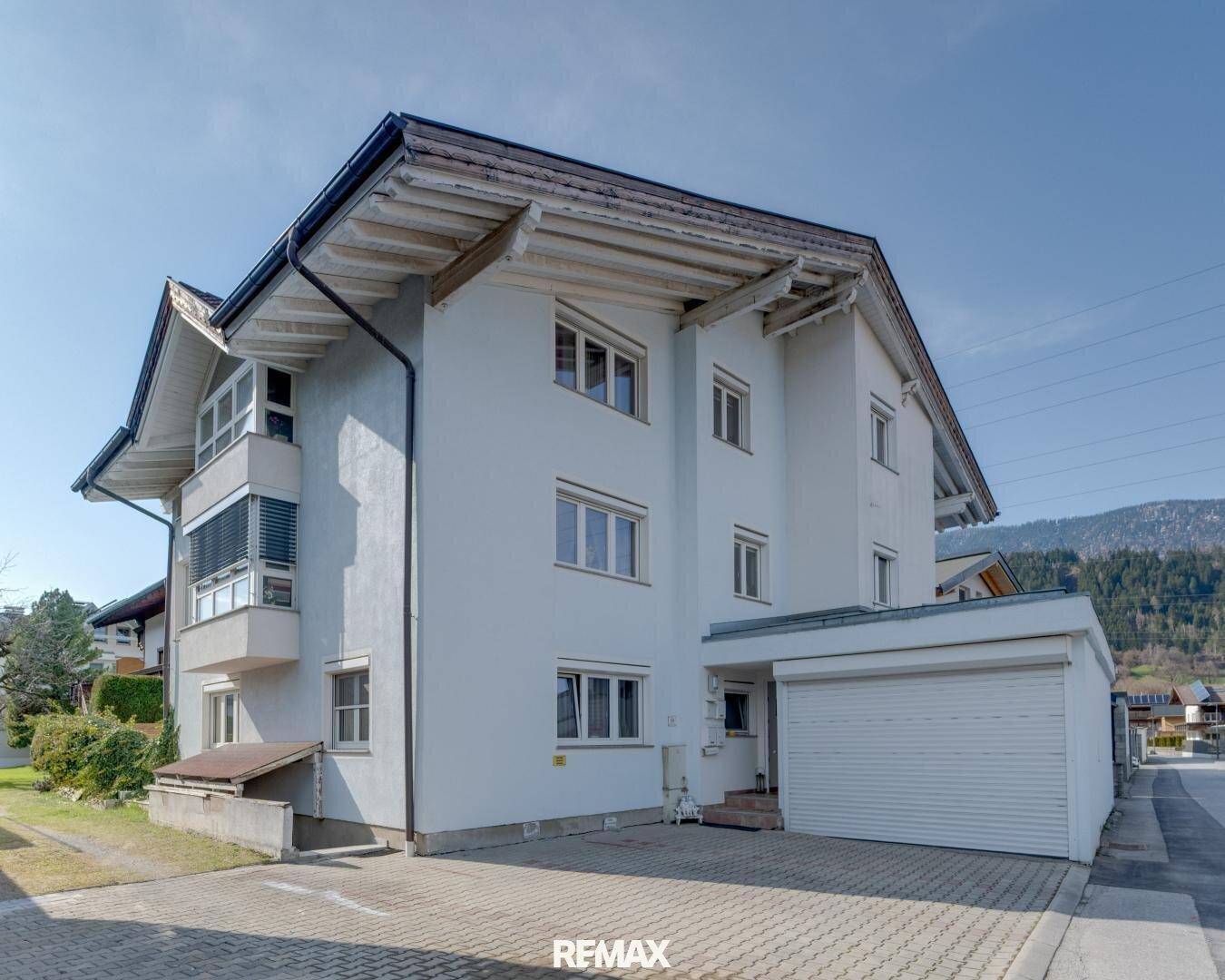 Gesamtansicht des Wohngebäudes mit Garage und gepflasterter Zufahrt unter blauem Himmel.