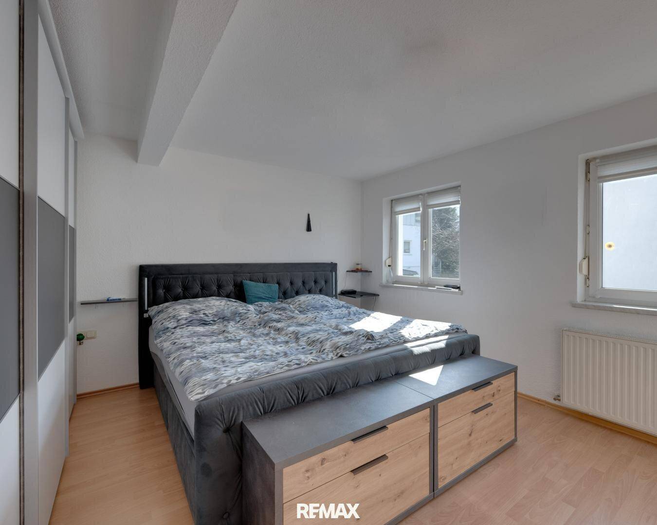 Helles Schlafzimmer mit großem Doppelbett, Einbauschränken und zwei Fenstern.