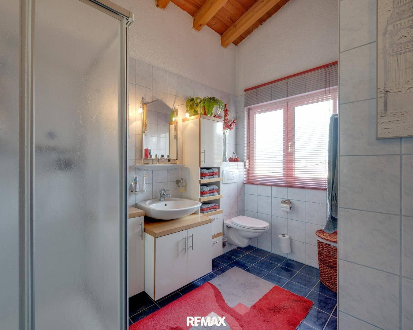 Badezimmer mit Duschkabine, WC, Waschtisch und Fenster unter Holzbalkendecke.