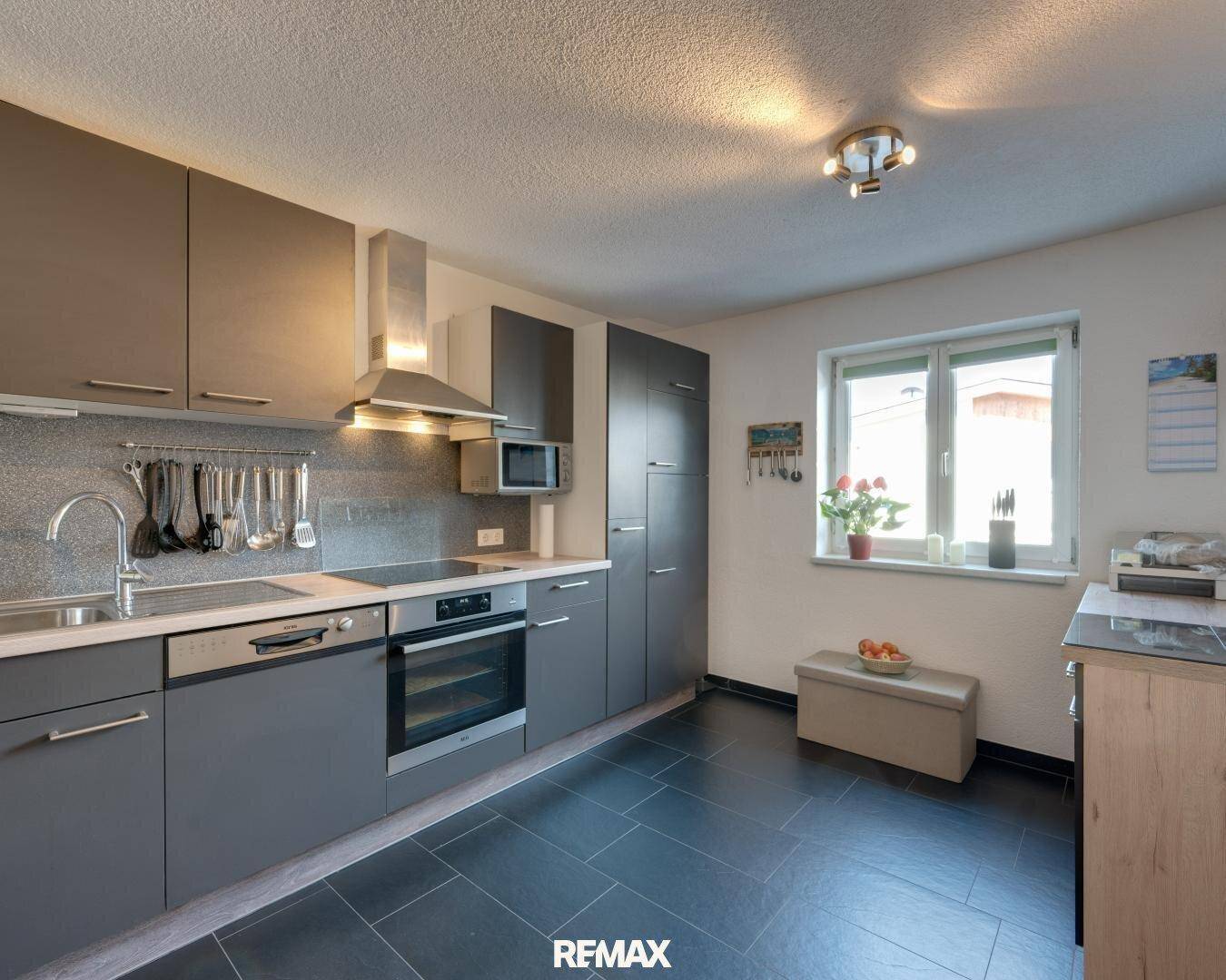 Moderne Küche mit grauen Schränken, dunklem Fliesenboden und Fenster für Tageslicht.