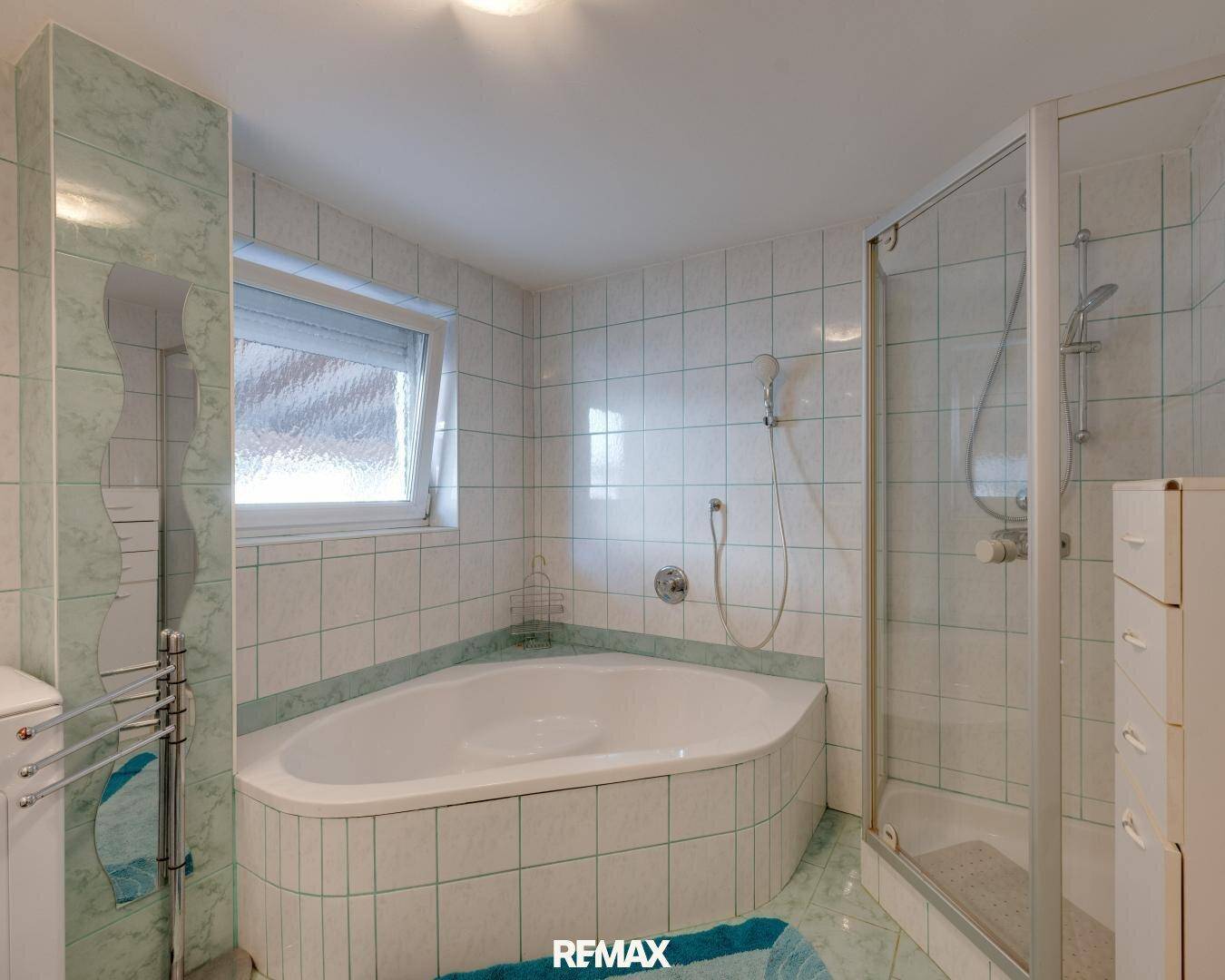 Badezimmer mit Eckbadewanne, Duschkabine und hellgrünen Fliesen an Wänden und Boden.