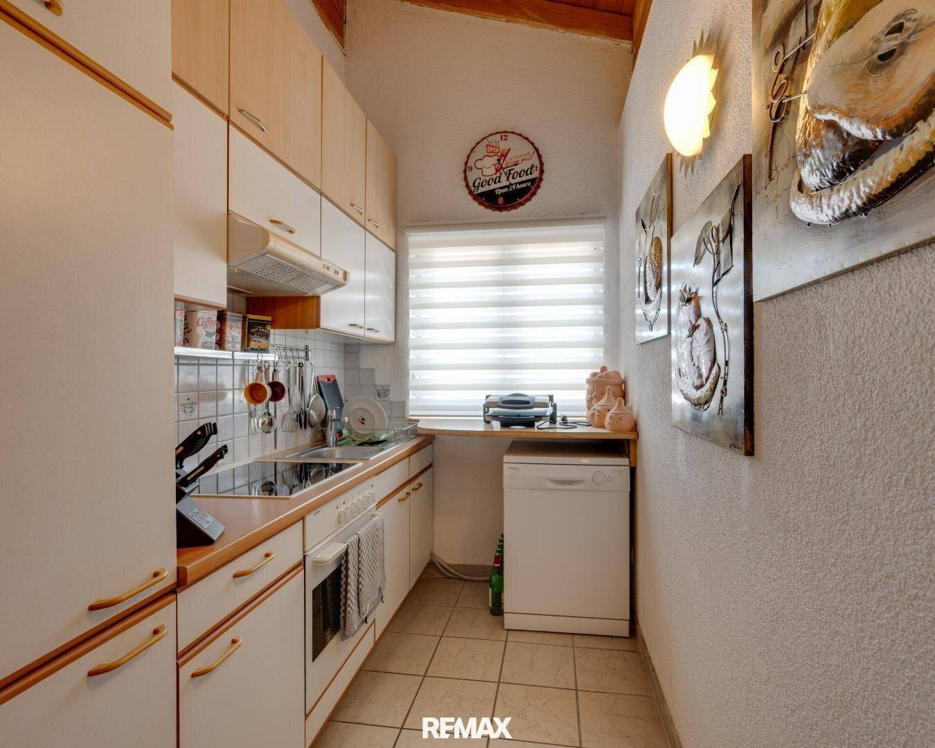 Schmale Küche mit weißen Einbauschränken, Fliesenboden und Fenster für Tageslicht.