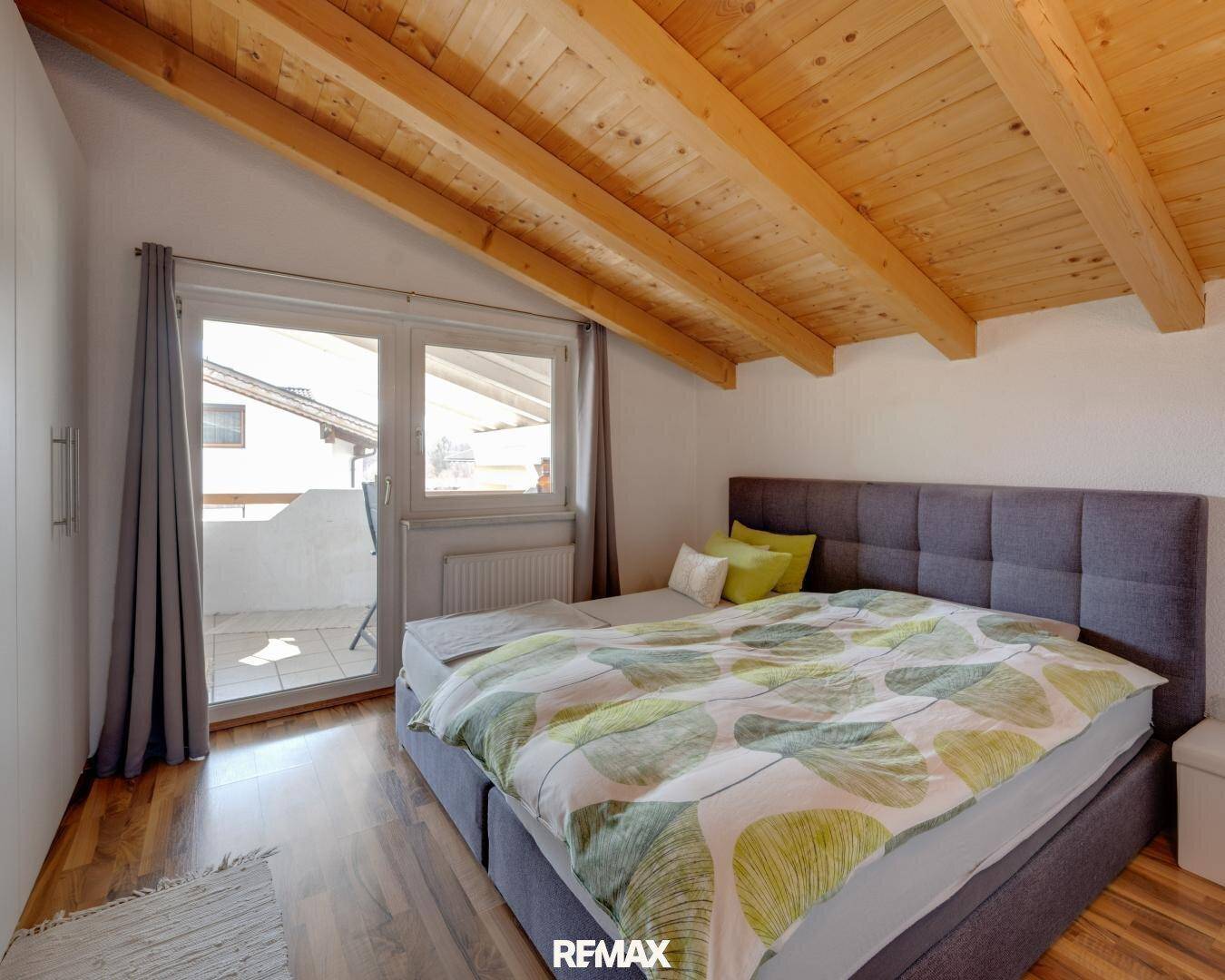 Schlafzimmer mit Holzbalkendecke und direktem Zugang zu einem sonnigen Balkon.