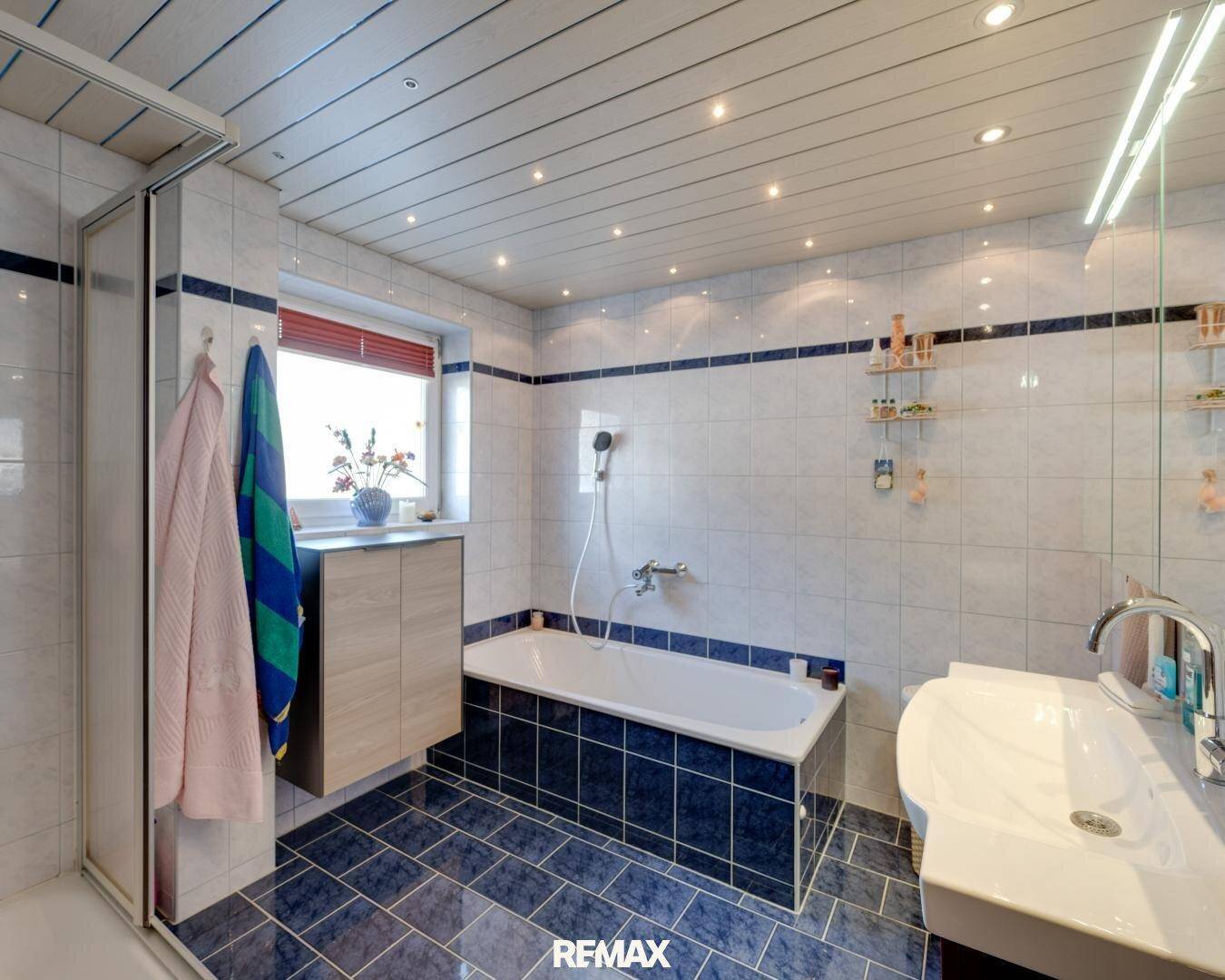 Badezimmer mit blauen und weißen Fliesen, Badewanne, Duschkabine und Einbauspots.
