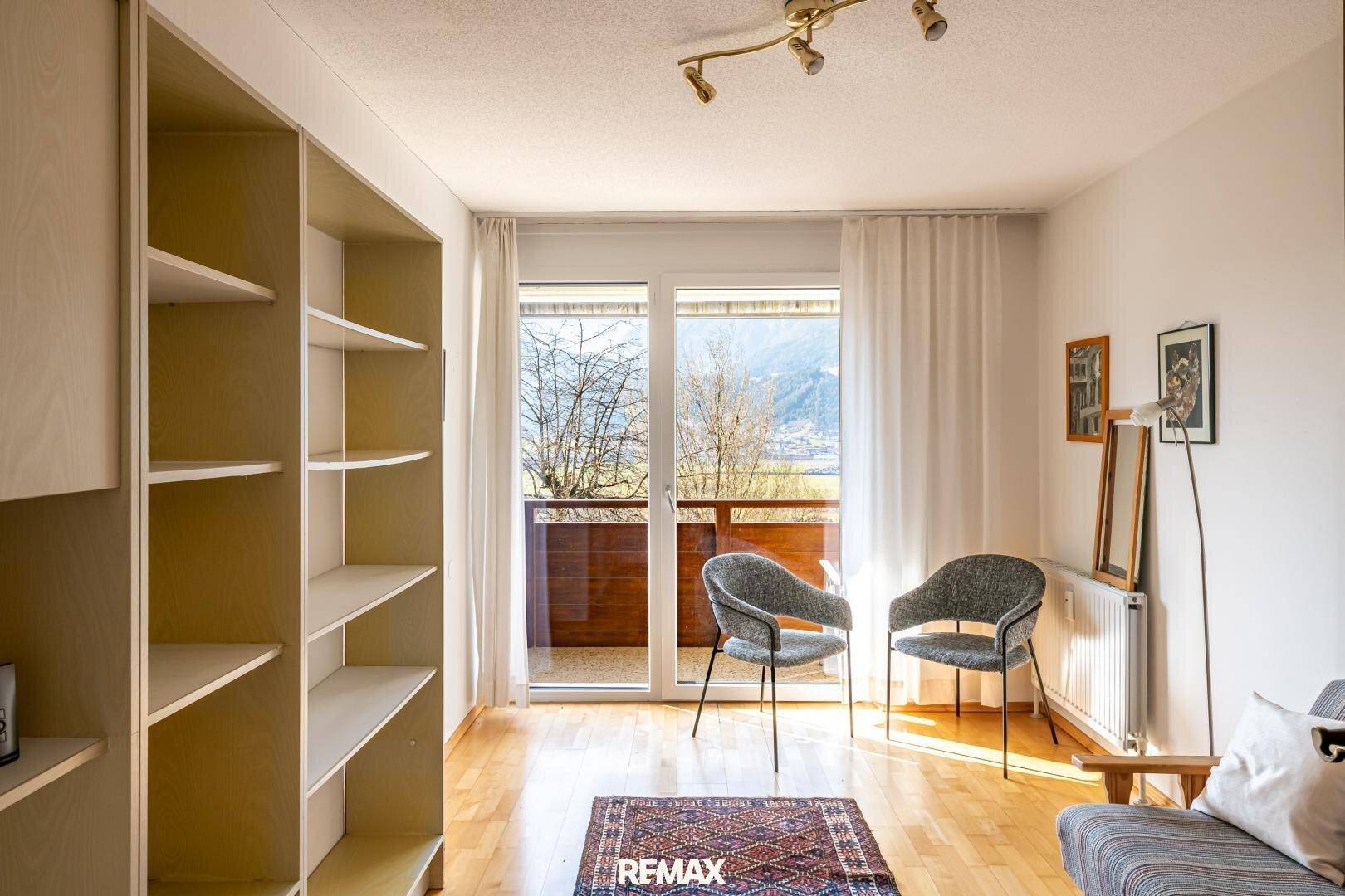 Helles Zimmer mit Parkettboden, Einbauregalen und Zugang zu einem Balkon.